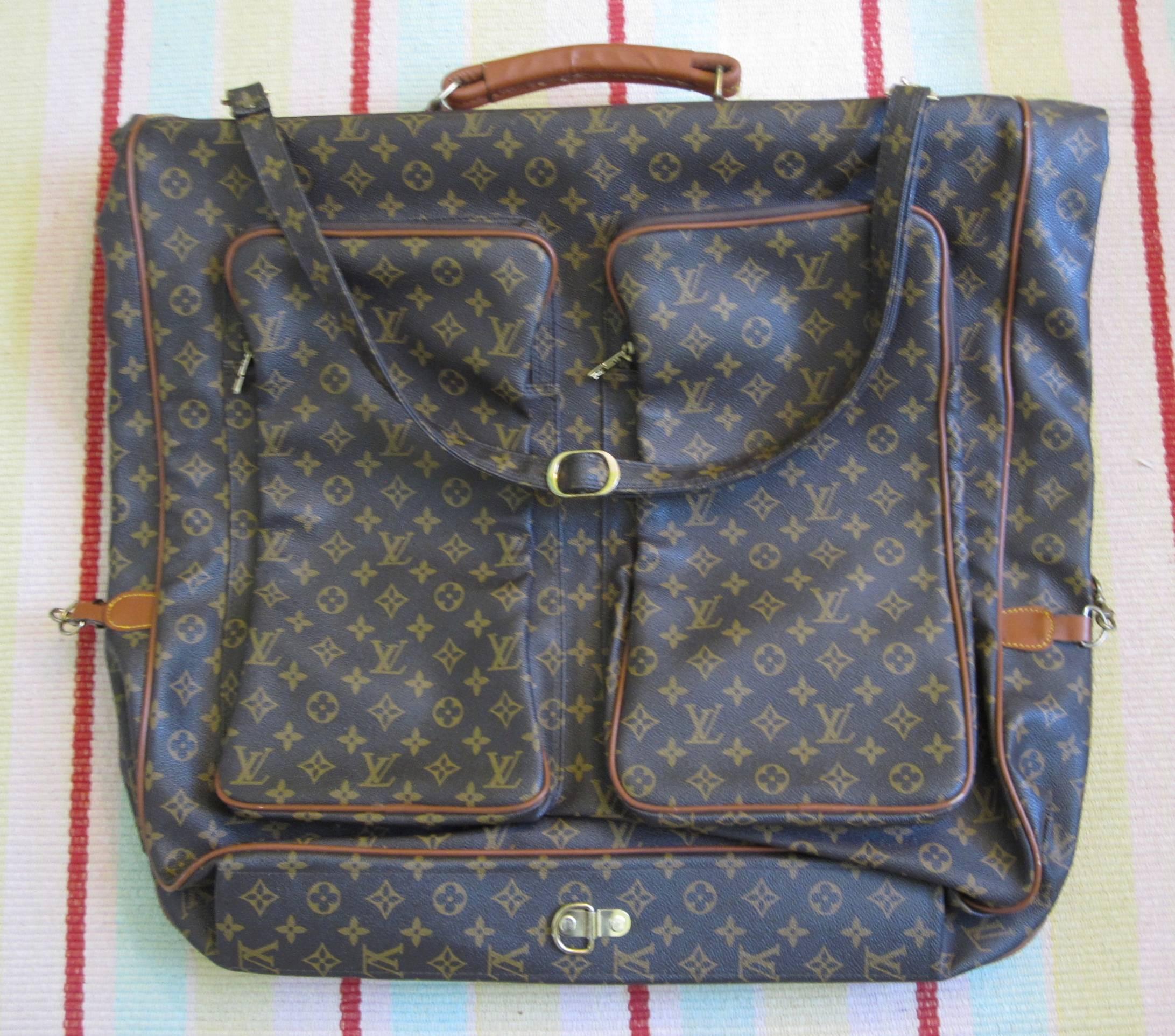 A vintage, iconic LV monogram Louis Vuitton fold-over large garment bag with four outer pockets. Equipped with a metal hanging hook under a flap cover showing a leather signature label. The bag is easily secured with two gold-tone spring latch hooks