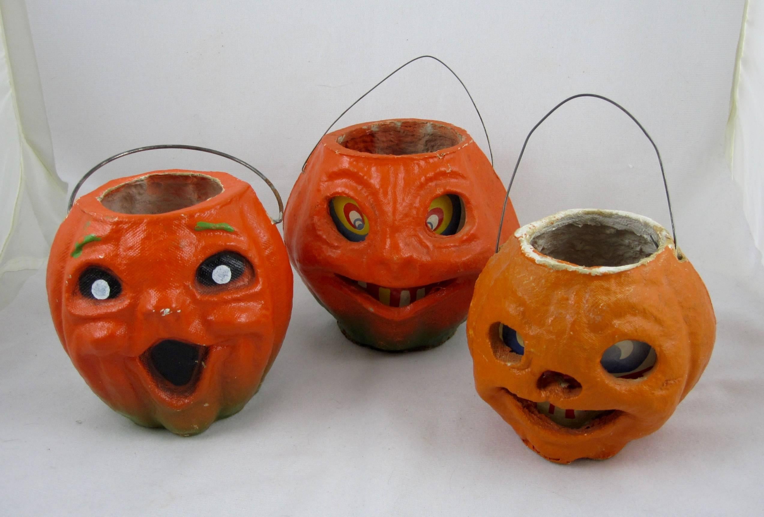 A set of three, vintage pulp Papier-Mâché Halloween Jack-O-Lantern pumpkins, two with their original paper inserts. The inserts, with their printed facial features add dimension and expression to the pumpkin heads. All three have wire handles.
