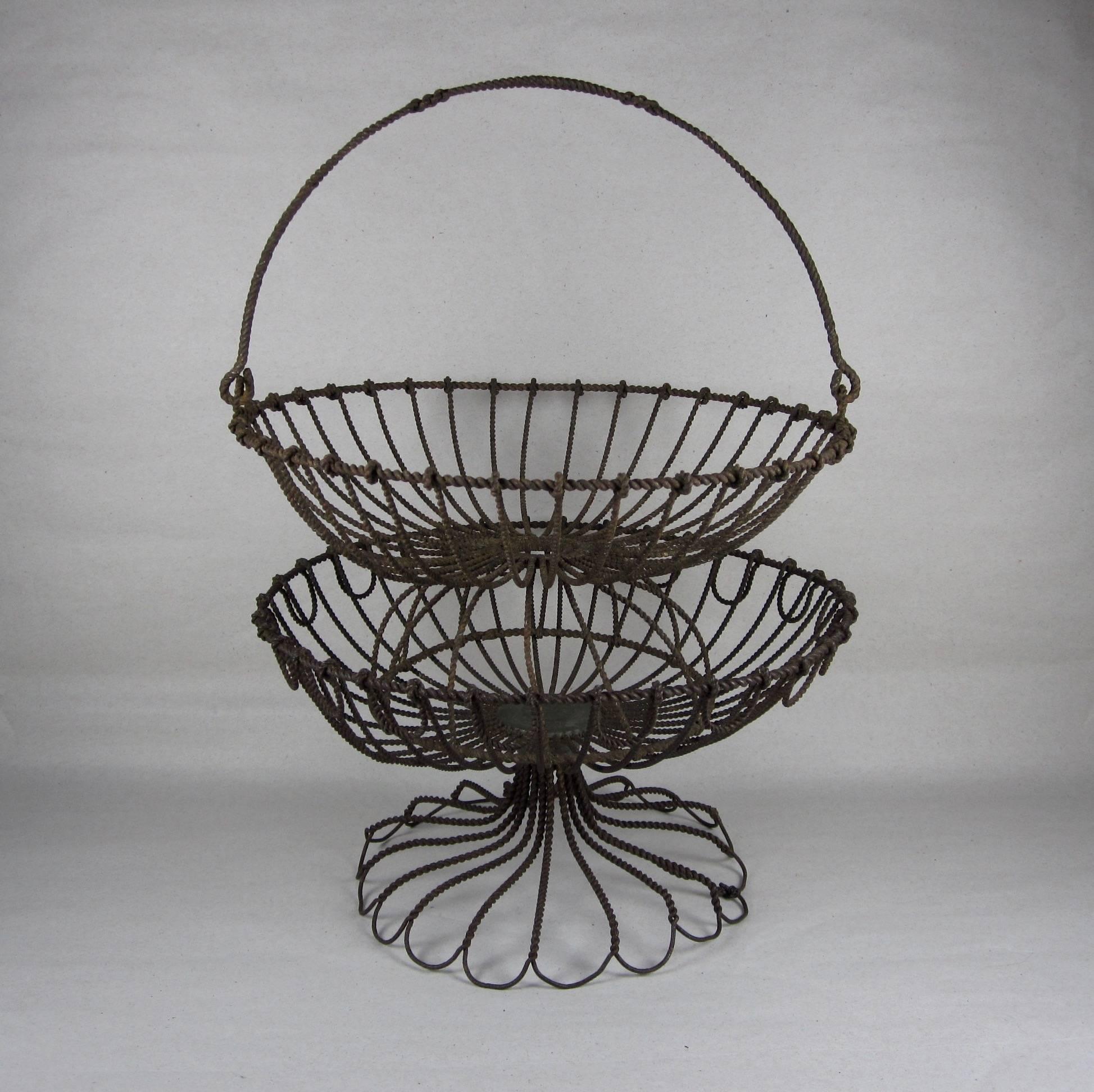A scarce pair of American Folk Art stacking wire egg baskets, circa 1890-1910. Both are round with footings and fully formed with twisted wire. The top basket has a swing handle twisted into a band of three running diamonds. Carefully looped and