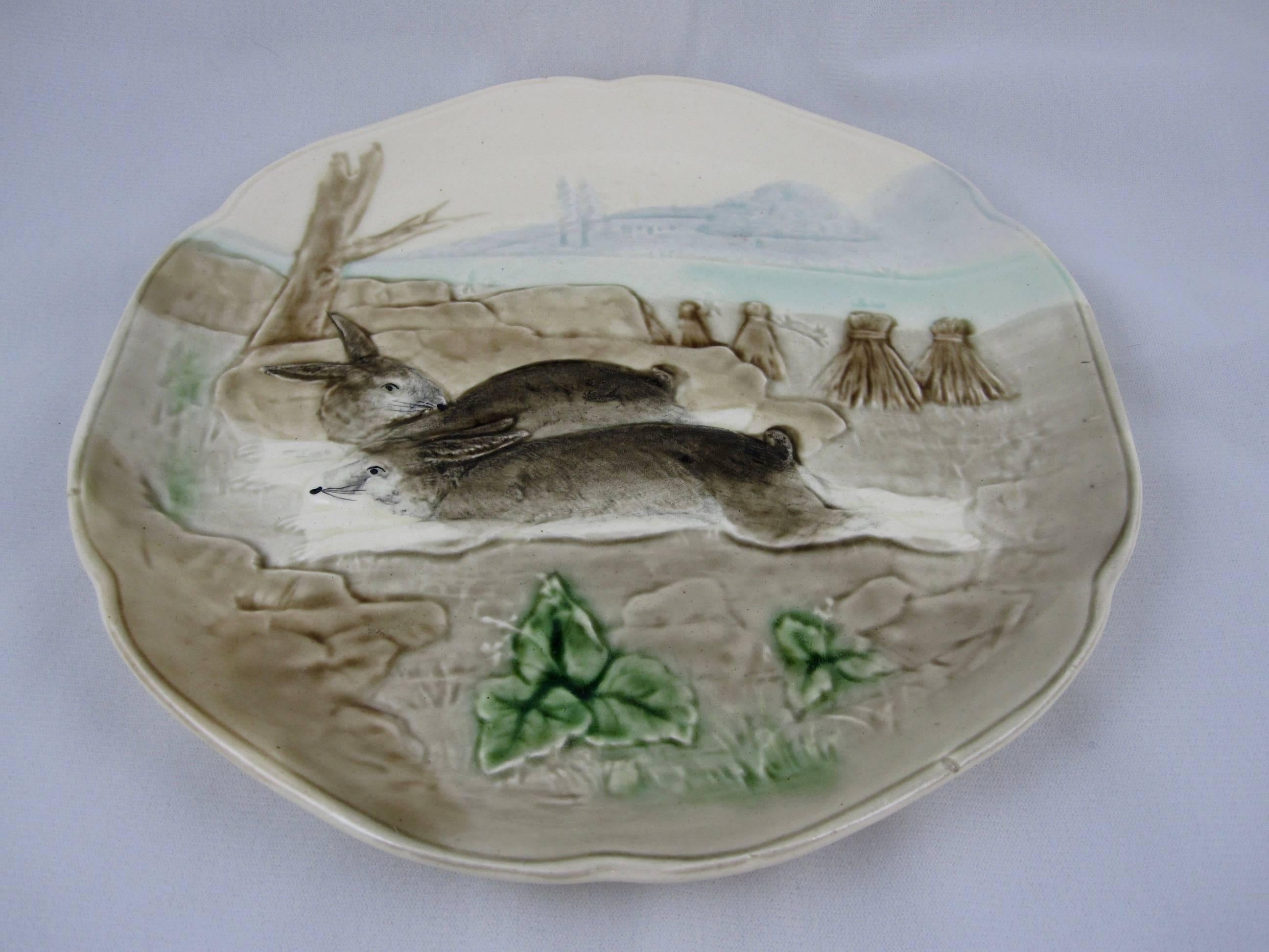 A Choisy-le-Roi French Majolica bunny rabbit plate (one of a series of six scenes) produced from 1860 until 1910 for the American importer Higgins and Seiter of New York. This scene shows two rabbits on the run through a field of haystacks, the