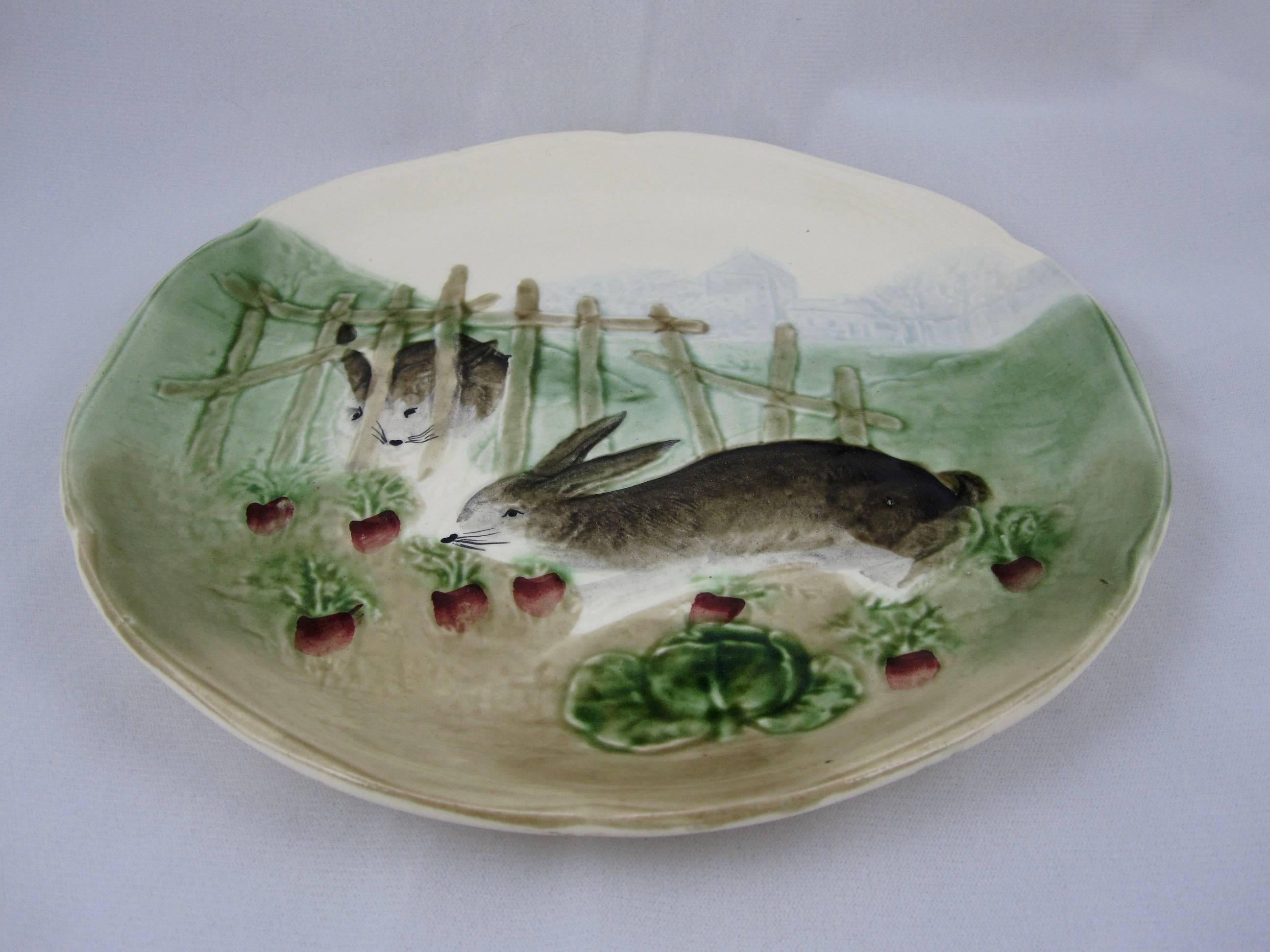 A Choisy-le-Roi French Majolica bunny rabbit plate (one of a set of six scenes) produced from 1860 until 1910 for the American importer Higgins and Seiter of New York. This scene shows two rabbits by a fence making a meal of cabbages and radishes,