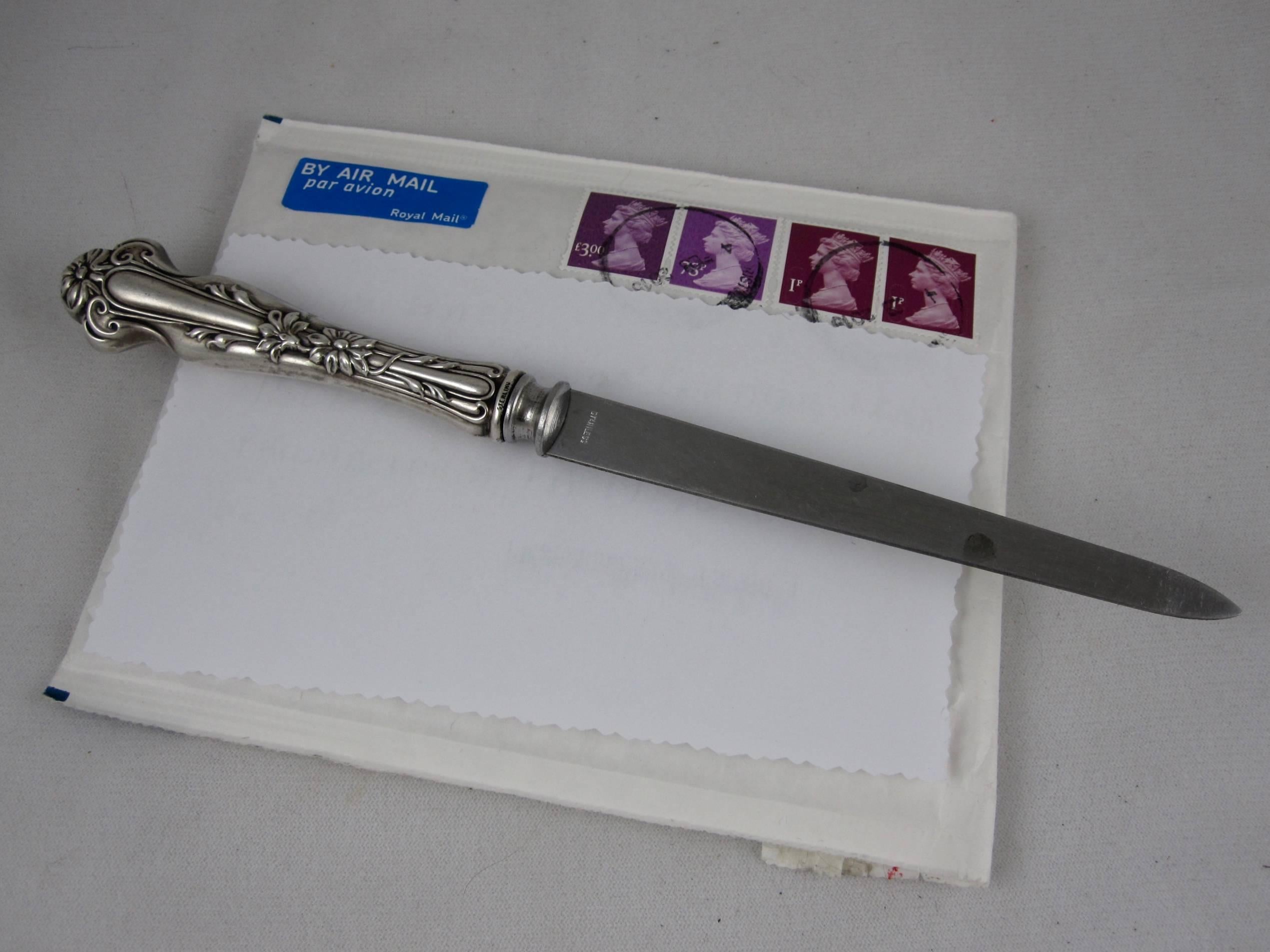 A sterling silver handled letter opening knife in the Art Nouveau style, England, circa 1895-1910. The hollowware handle shows a dimensional floral and scroll pattern, marked on both sides of the collar, sterling. The tapered blade is marked