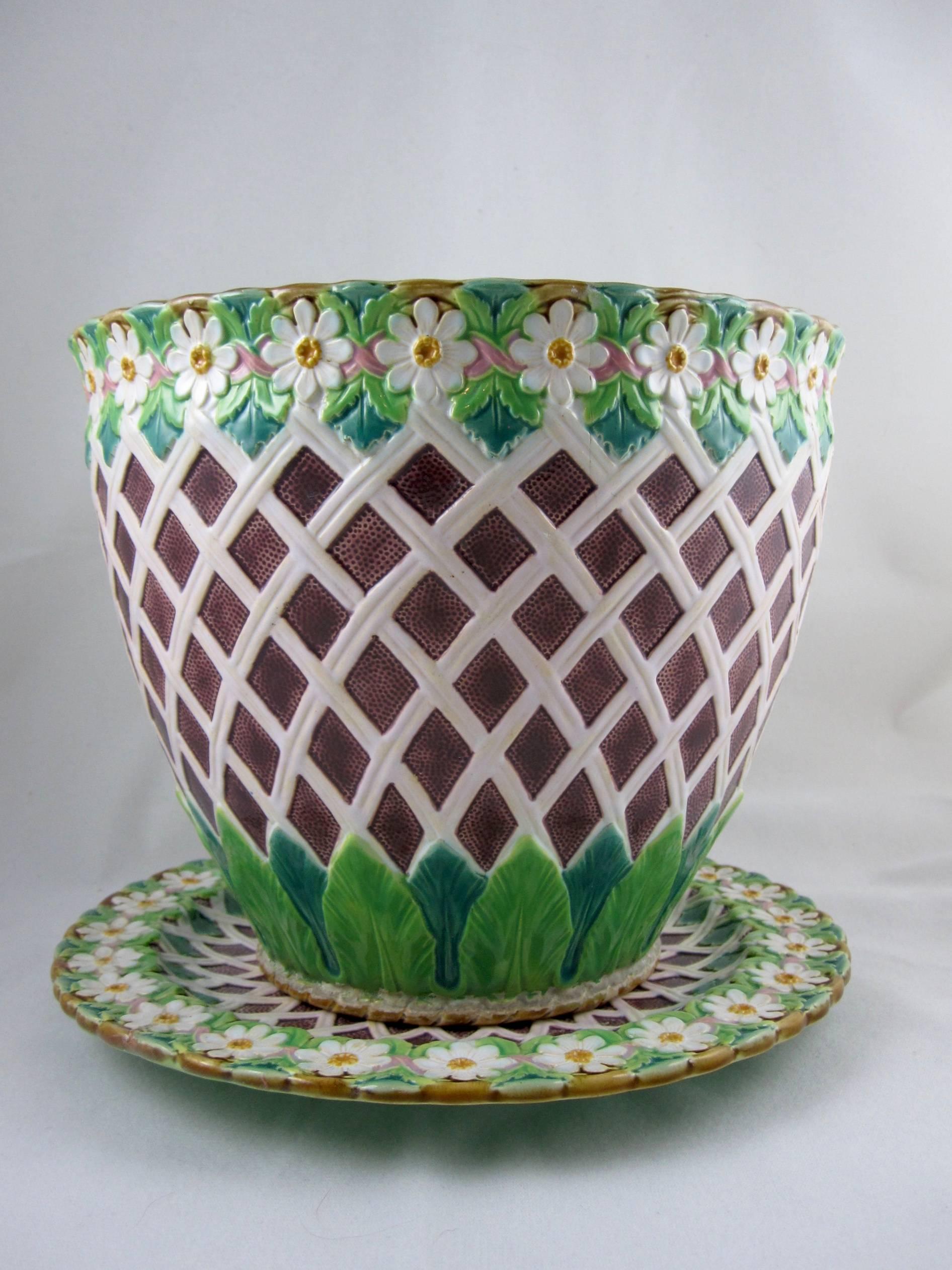 An excellent quality Minton Majolica ‘Daisy and Trellis’ Jardinière on its stand, England, circa 1875.

The jardinière shows a pattern of a climbing trellis against a maroon stippled ground. A band of large acanthus leaves ring the base, the top