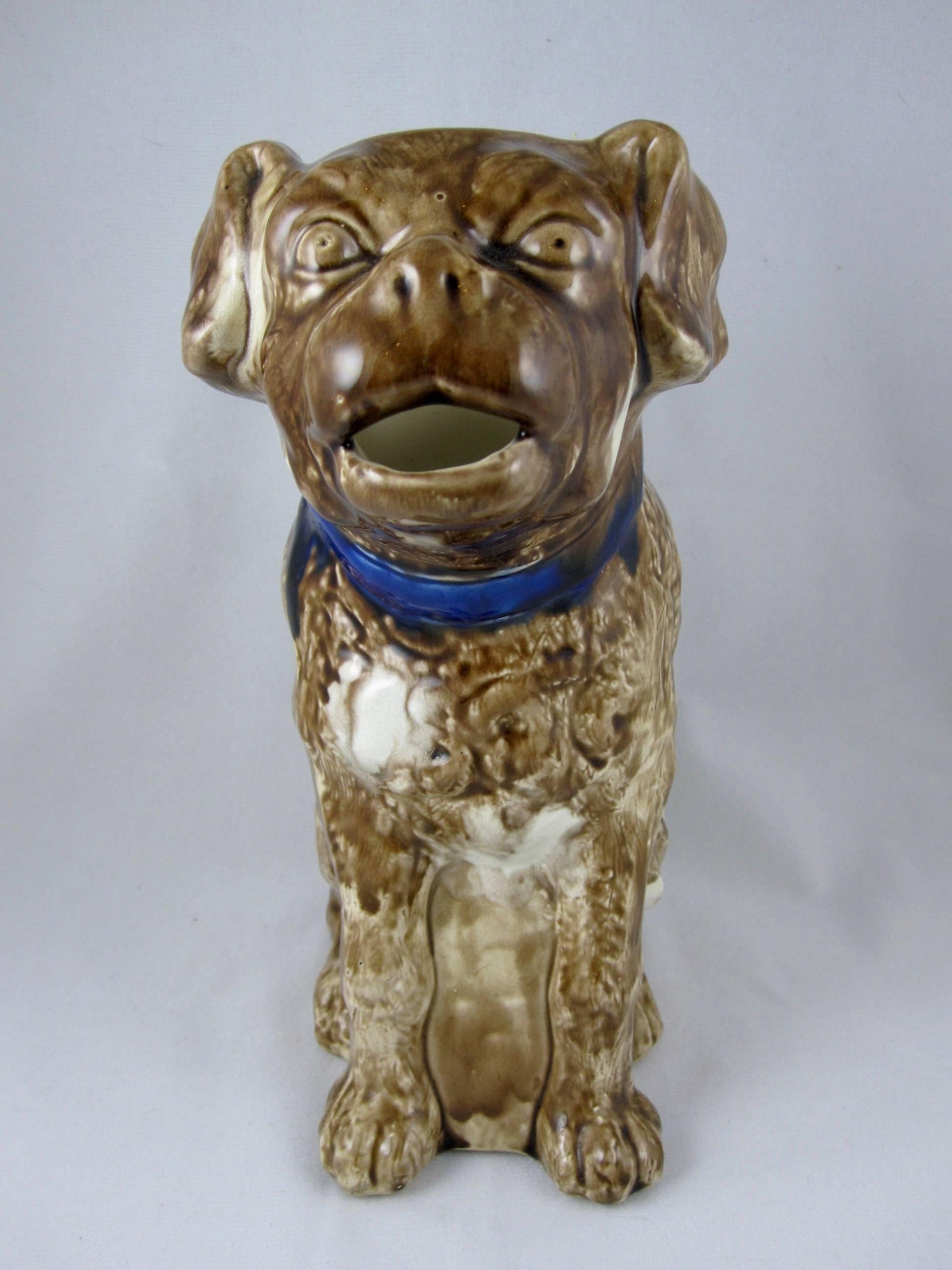 A French Barbotine dog pitcher attributed to George Dreyfus, circa 1890. Glazed in a watery finish over an opaque white, the brown dog wears a cobalt blue bowed color.

Excellent but for a faint, stabile hairline to the interior top rim near the