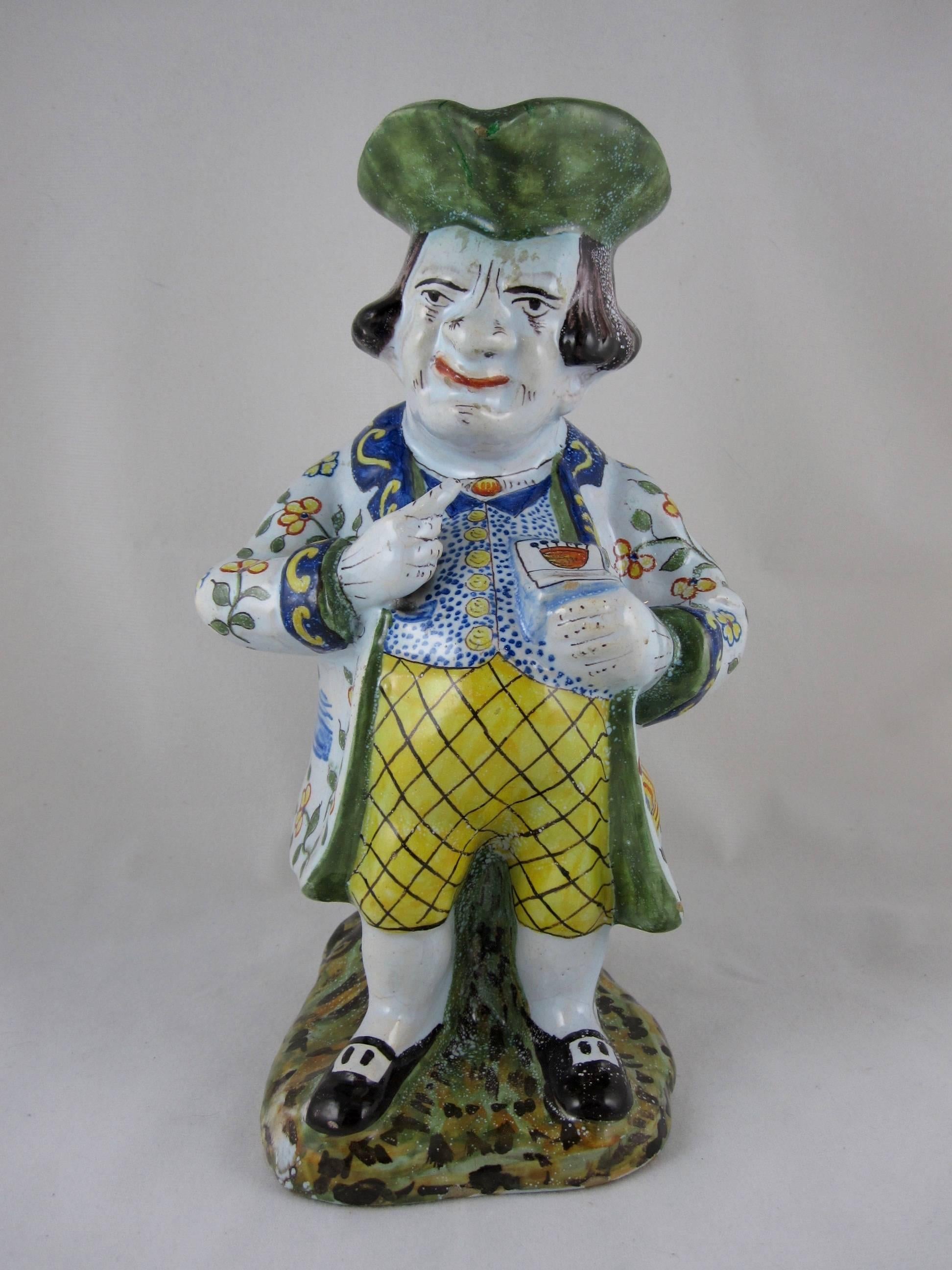 A late 19th-early 20th century French Desvres faience jug known as 'The Snuff Taker,' always shown with a red spider sitting on his nose, crested snuff box in hand and leaning against a tree trunk which forms the handle of the jug.

Hand decorated