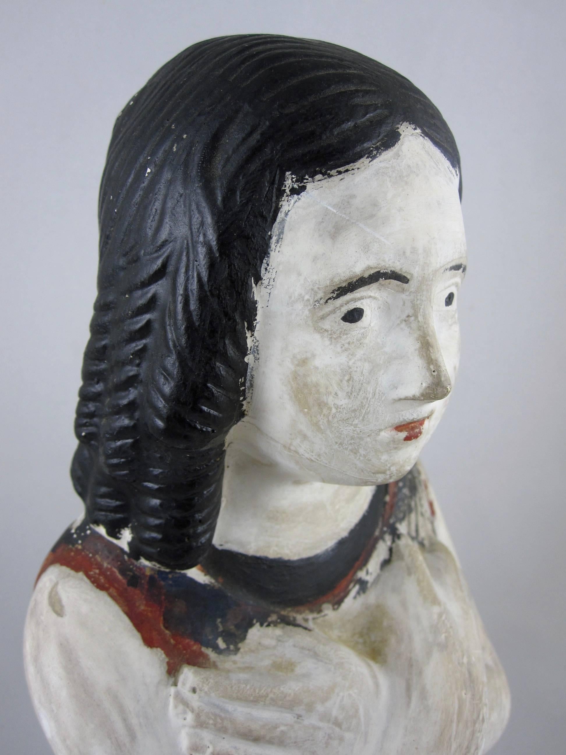 A mid-19th century Pennsylvania Chalkware bust, a figure of a girl. Highlighted with the original polychrome painting, this charming figure has a naive facial expression. The girl has her arms crossed across her chest and her hair is set in deep