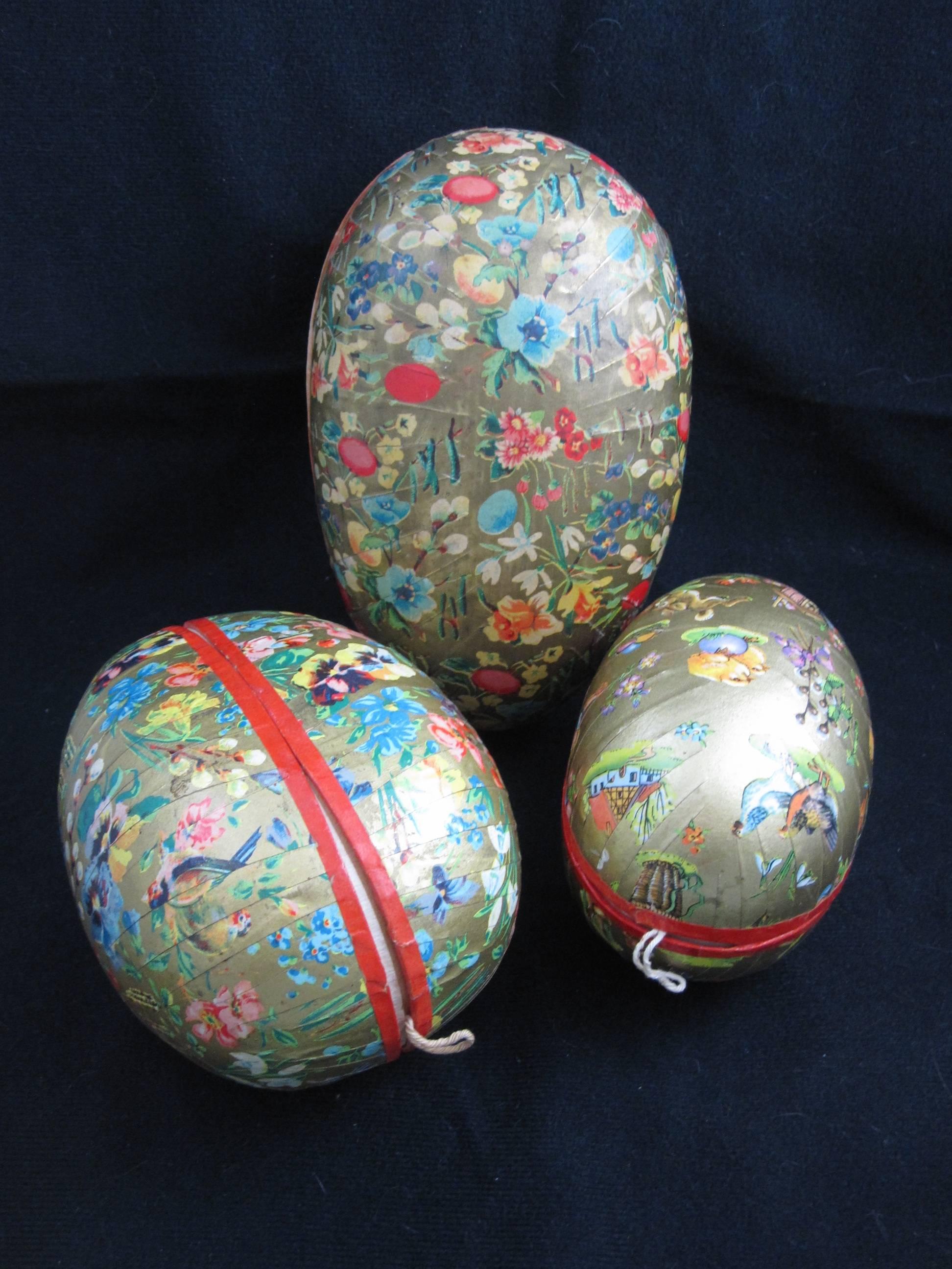 Popular during the Victorian era, this group of three German made papier-mâché egg-shaped Holiday candy containers or ornaments are covered with goldtone paper showing images of spring flowers, birds, bunnies, and children. 

Made to hang on a