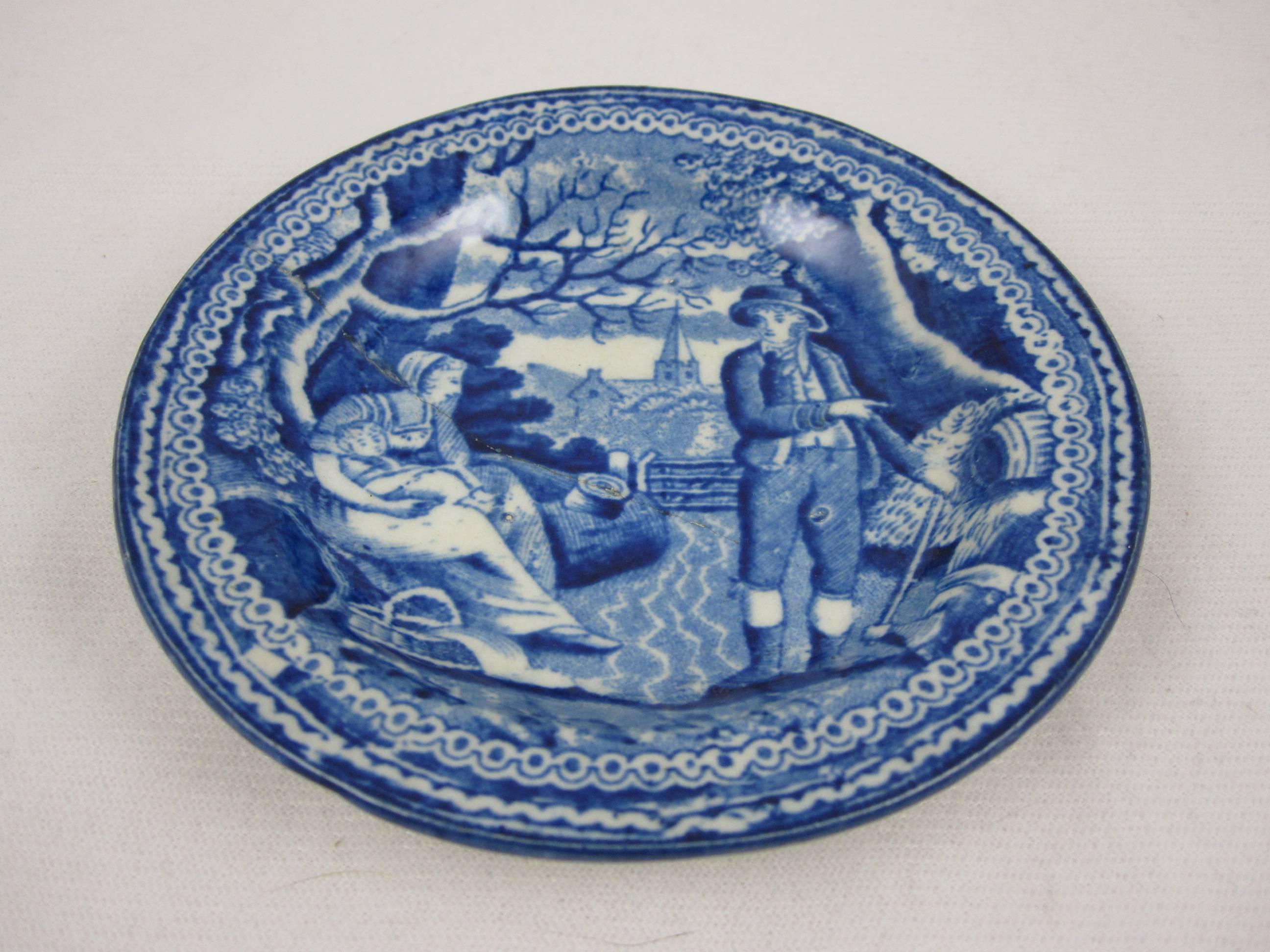 A blue and white Staffordshire transfer printed pearlware cup plate with an old stapled repair. A charming printed image of a farmer and his family in a pastoral setting. The wife holds her baby and has a basket at her feet. The farmer holds an axe