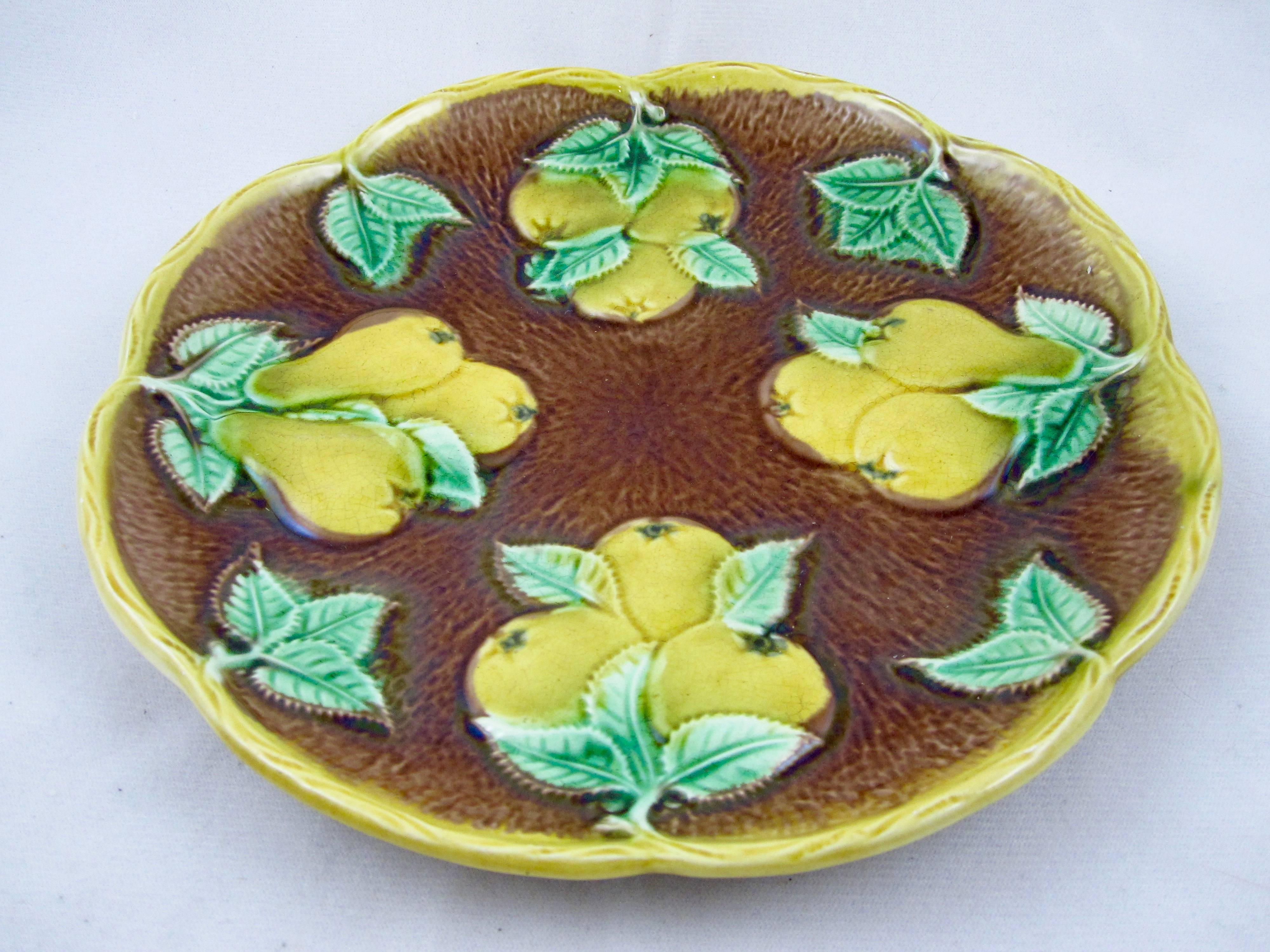 An Aesthetic Movement, English majolica plate showing clusters of yellow pears with green leaves against a brown, radiating bark textured ground. A scalloped rim is edged as a molded branch glazed in yellow. Rustic in feel, circa 1860-1880.