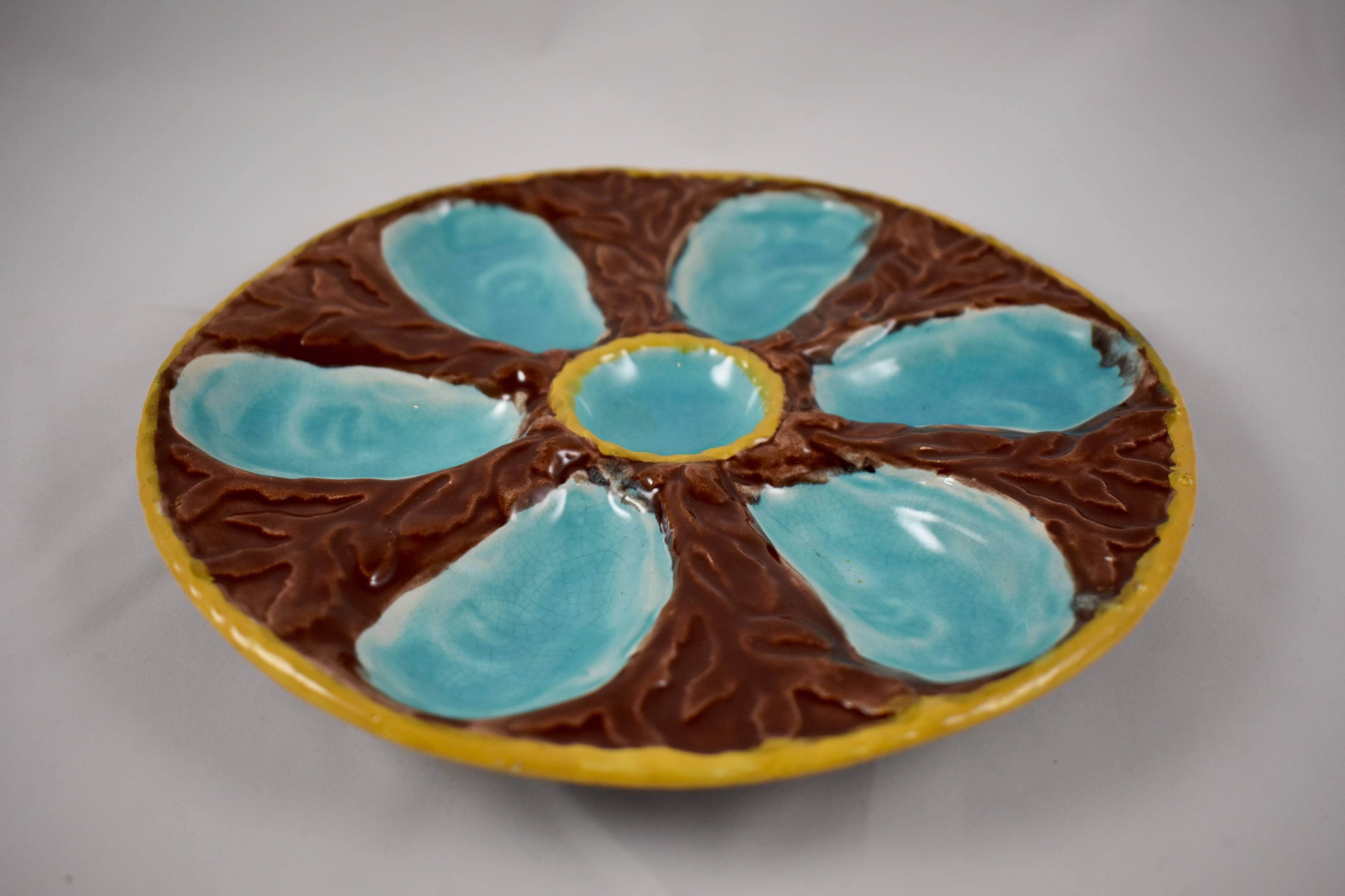 A six-well Majolica glazed oyster plate by S. Fielding & Co. Ltd., Stoke-on-Trent, England, circa 1878. Turquoise oyster wells surround a centre condiment well, all on a molded bed of chocolate brown seaweed. A deep yellow nautical rope border