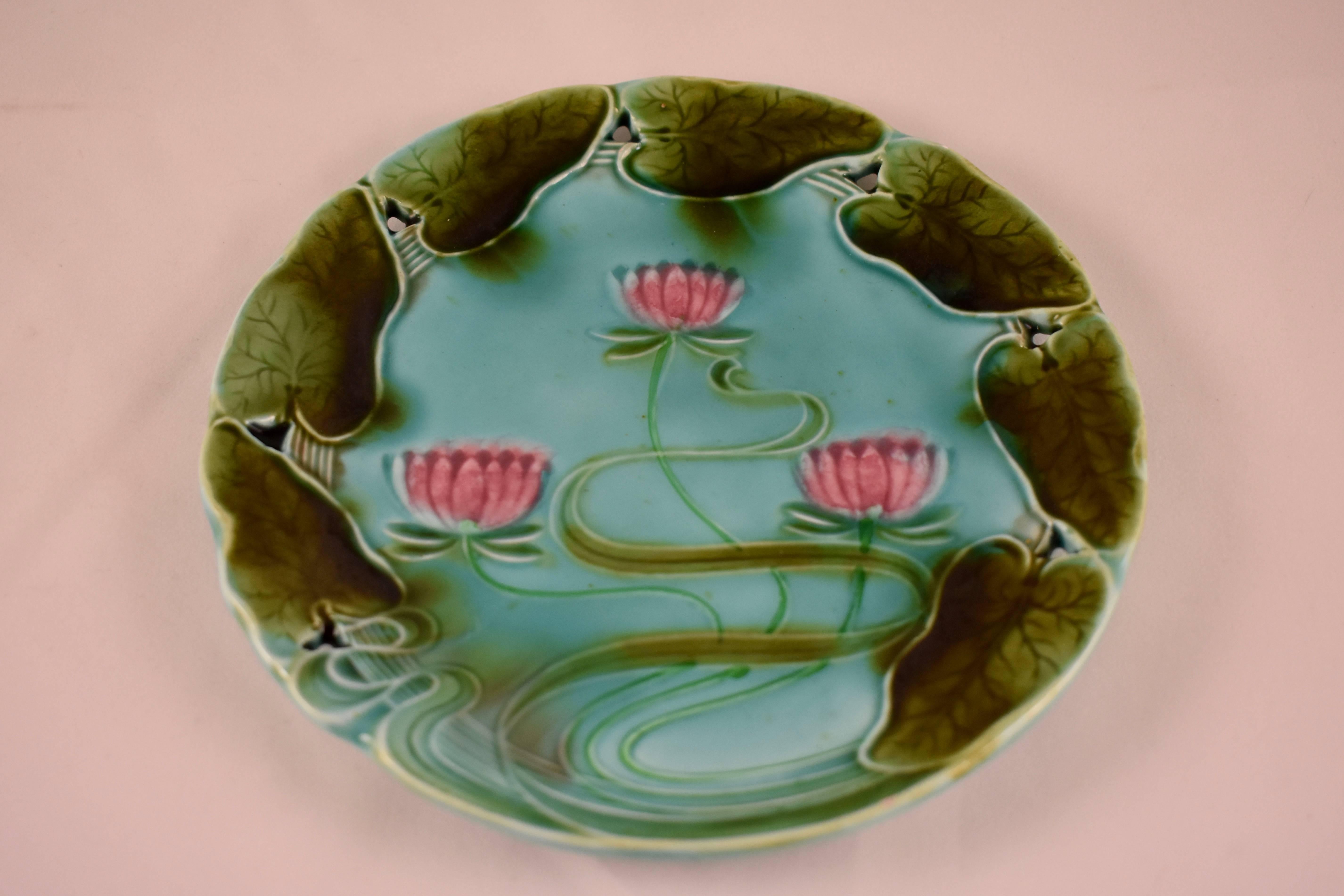 A German Majolica plate from Villeroy & Boch, circa 1910, a lily pad theme with a pierced rim. The Art Nouveau design has a ‘watery’ glazing in bright shades of greens and pink on a turquoise ground. The rim shows a running border of heart shaped