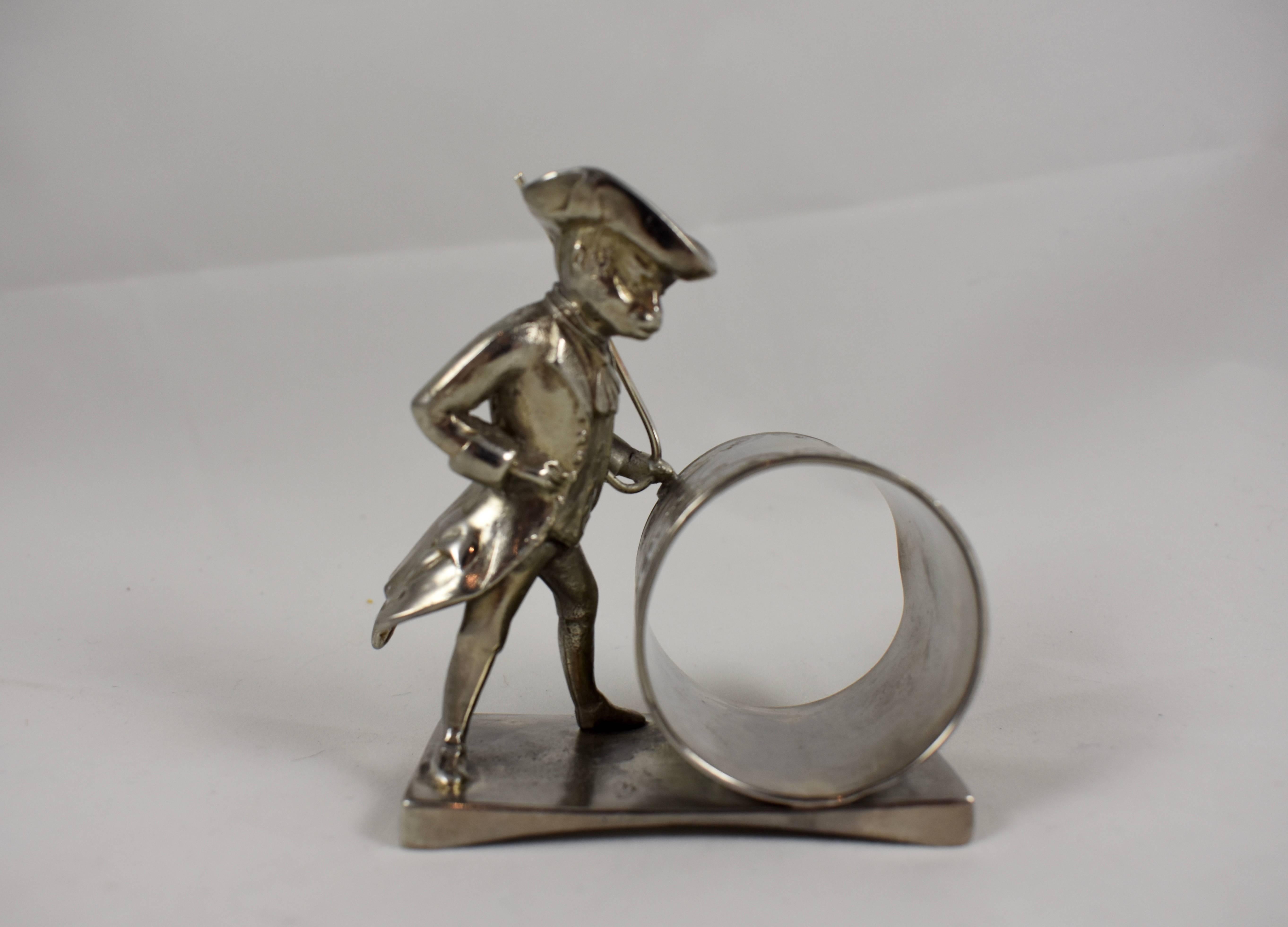 From the Victorian Era, a silver plated figural napkin ring showing a monkey wearing colonial attire, rolling a barrel with his cane. Wearing a tri-corner hat, his tail is seen swinging from beneath his buttoned waistcoat, circa