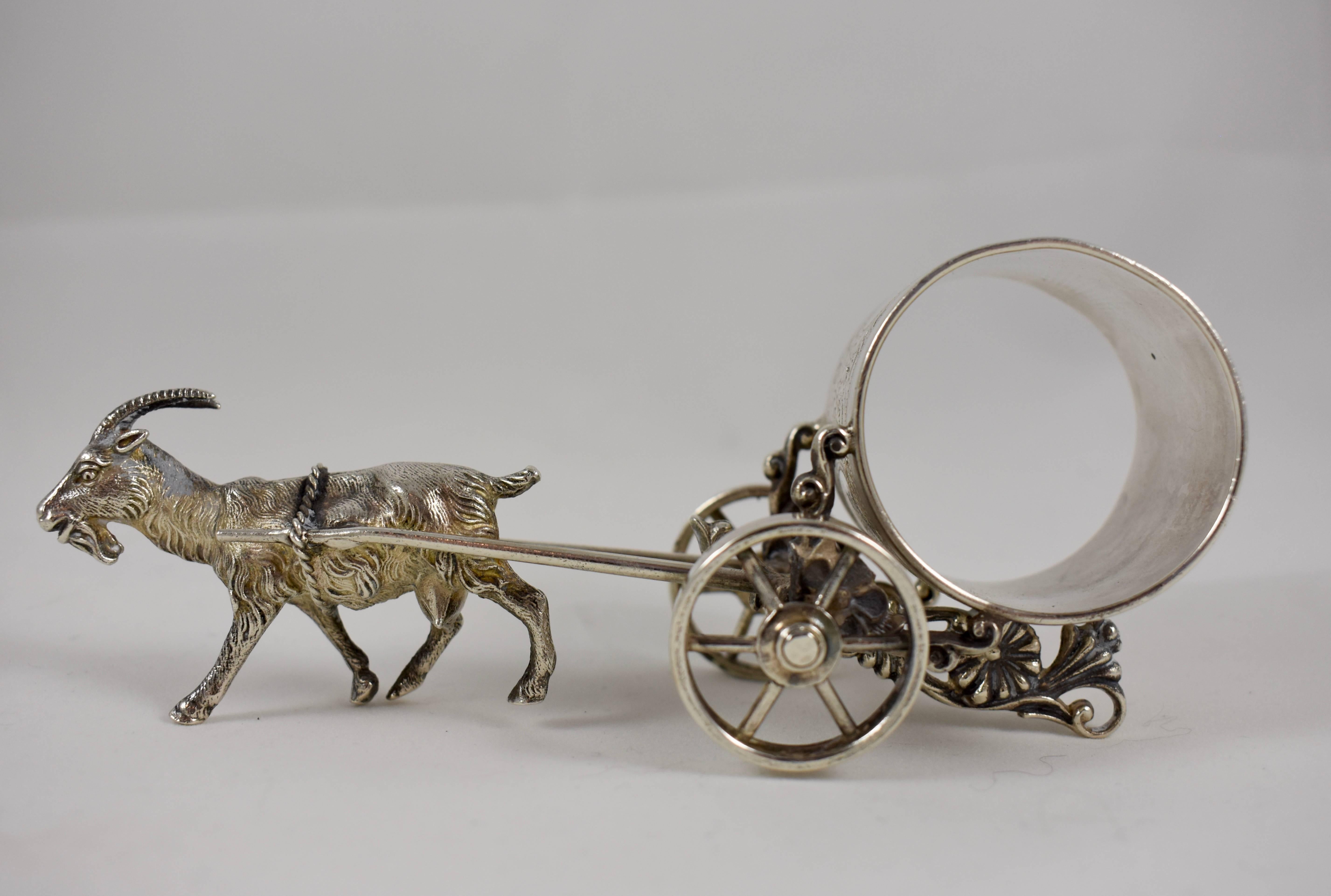 From the Victorian era, a silver plated figural napkin ring showing a horned goat pulling a cart holding the engraved ring. The wheels on the cart are functional. The ring is initial, great detail to this piece, circa 1885-1910. Unmarked.

The