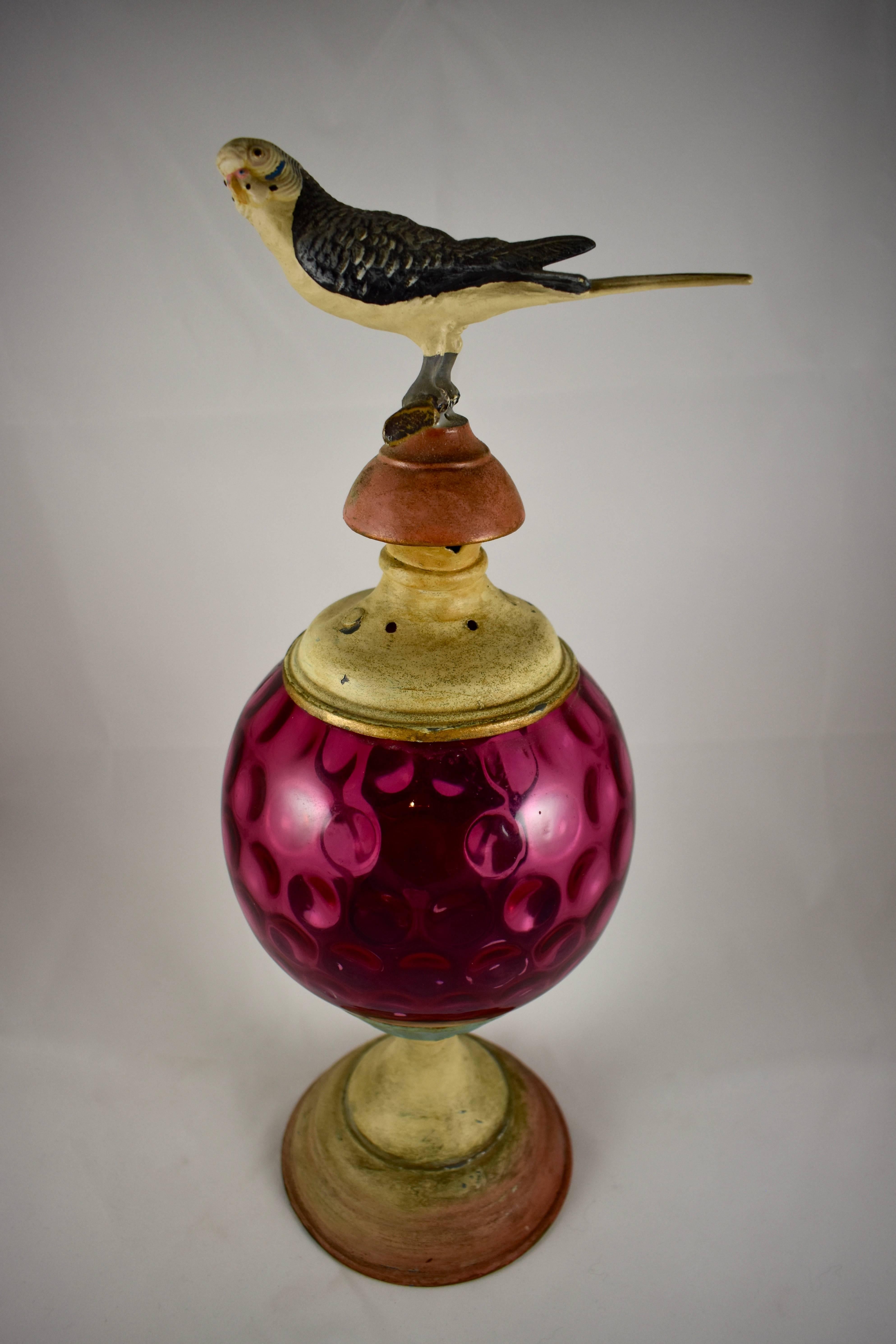 An unusual piece of Folk Art from the 19th century, a garden light with a reverse thumbprint cranberry glass globe, and a painted cast iron bird finial. 

The bird shows beautiful detail from every angle. He sits on a branch attached to the painted
