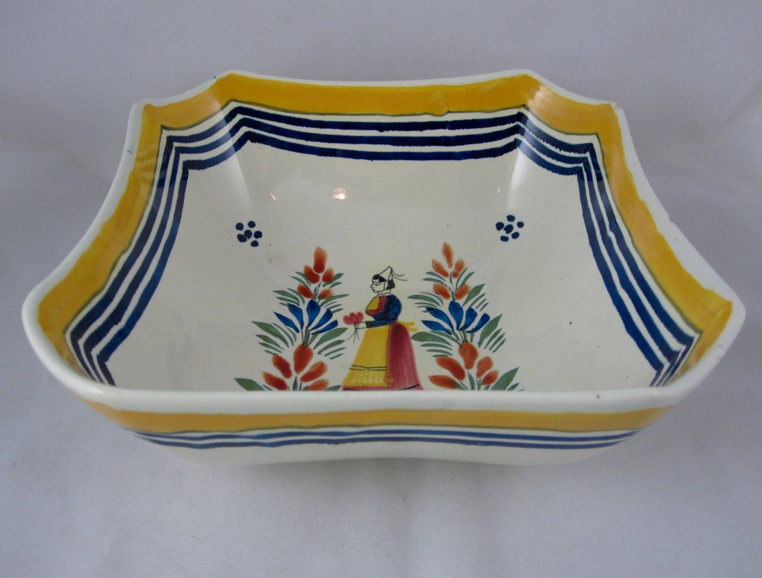 A Mid-Century French Faiençe deep square shaped serving bowl, signed Henriot Quimper France, mold no. 575. 

 A central sujet ordinaire image of a Breton woman, the femme de la Campagne, wearing traditional dress, holding a flower and standing