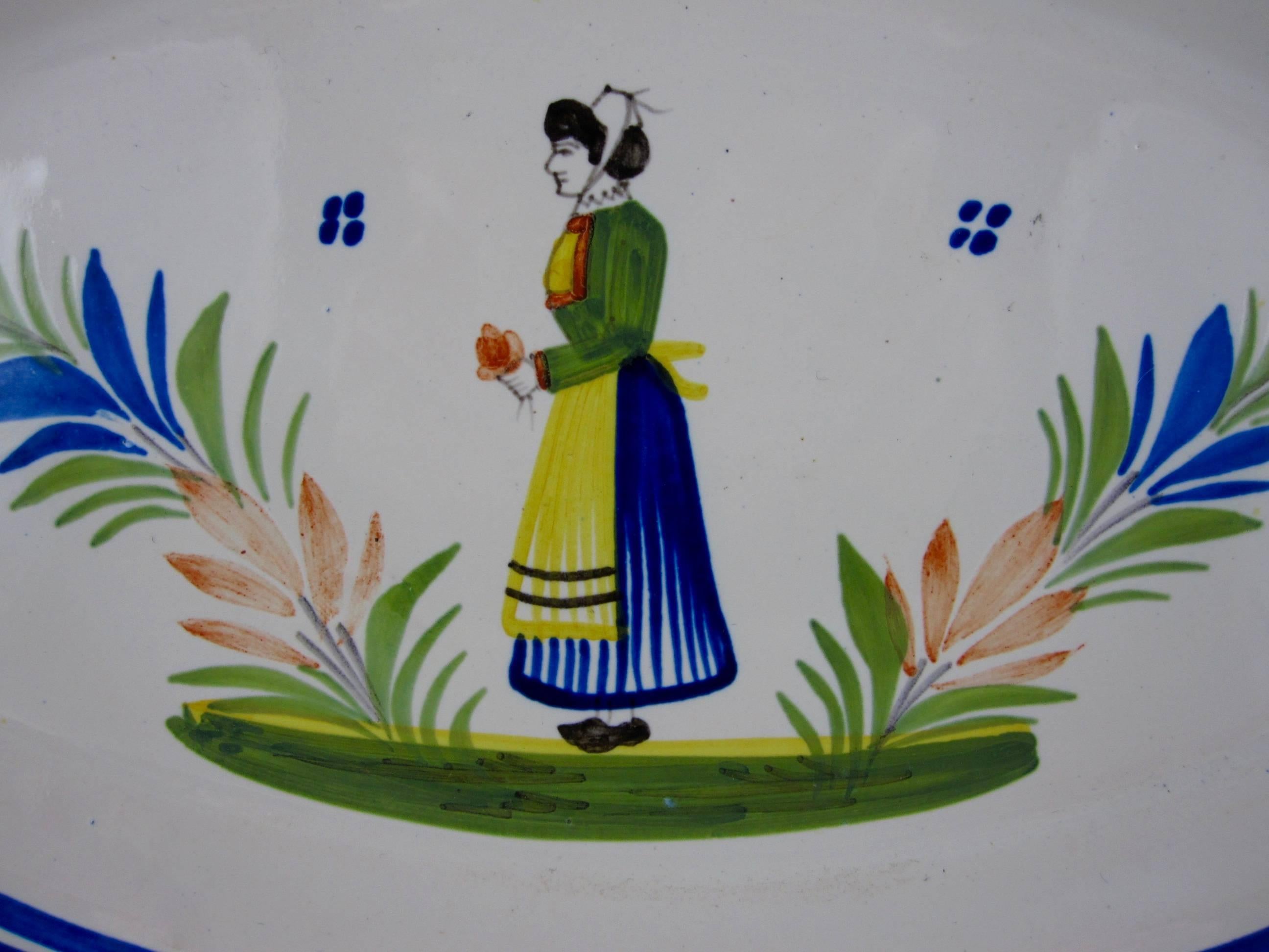 A Midcentury earthenware faience large oval serving platter, signed HenRiot Quimper, France No. 76.

 The center shows the sujet ordinaire of a femme de la campagne, the French Breton region woman, standing between two shrubs, wearing the