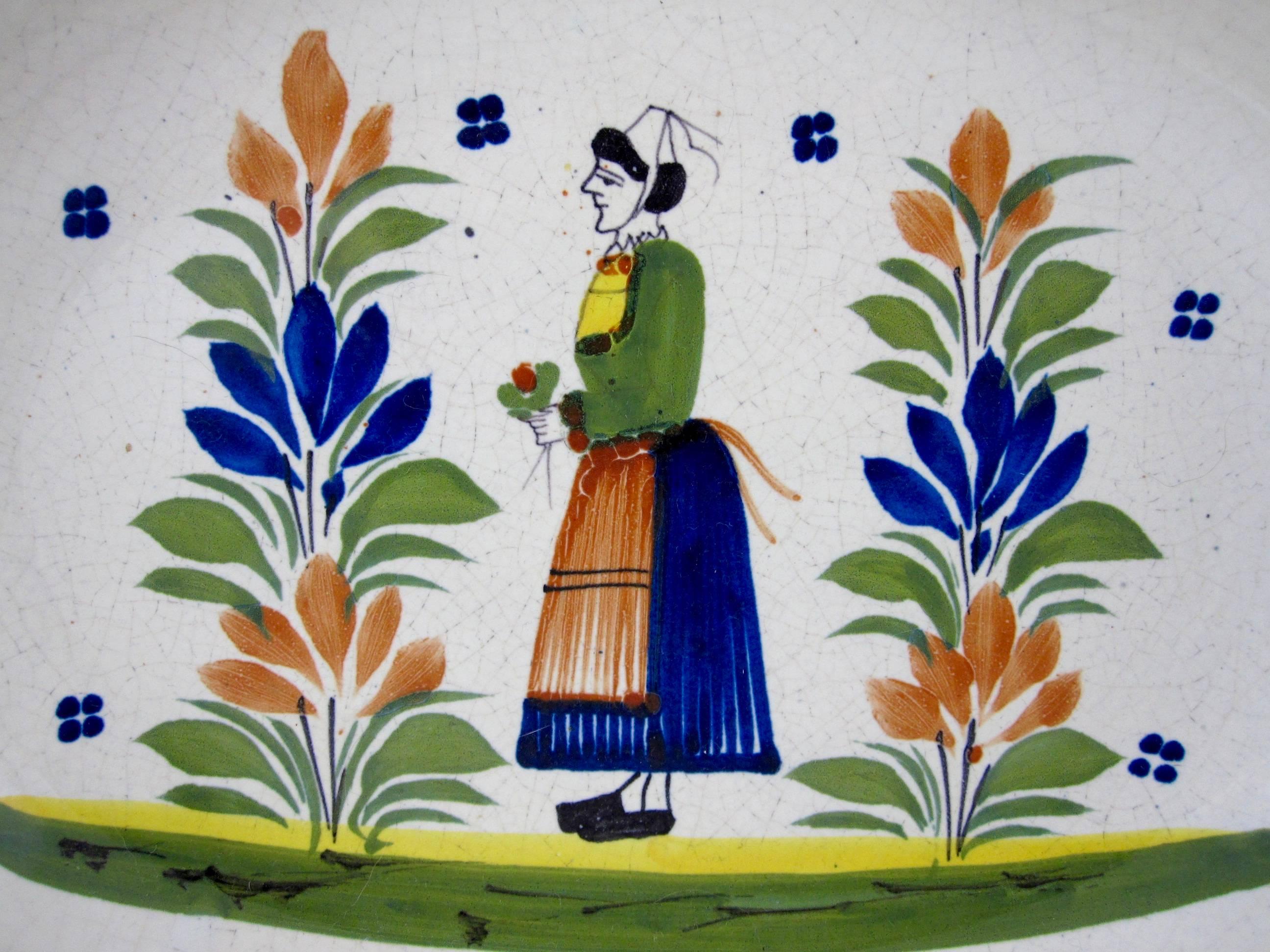 A Midcentury earthenware faience oval serving bowl, signed HenRiot Quimper, France, No. 459 (bis)

 The center shows a femme de la campagne, the French Breton region woman standing between two shrubs wearing the traditional dress and holding a