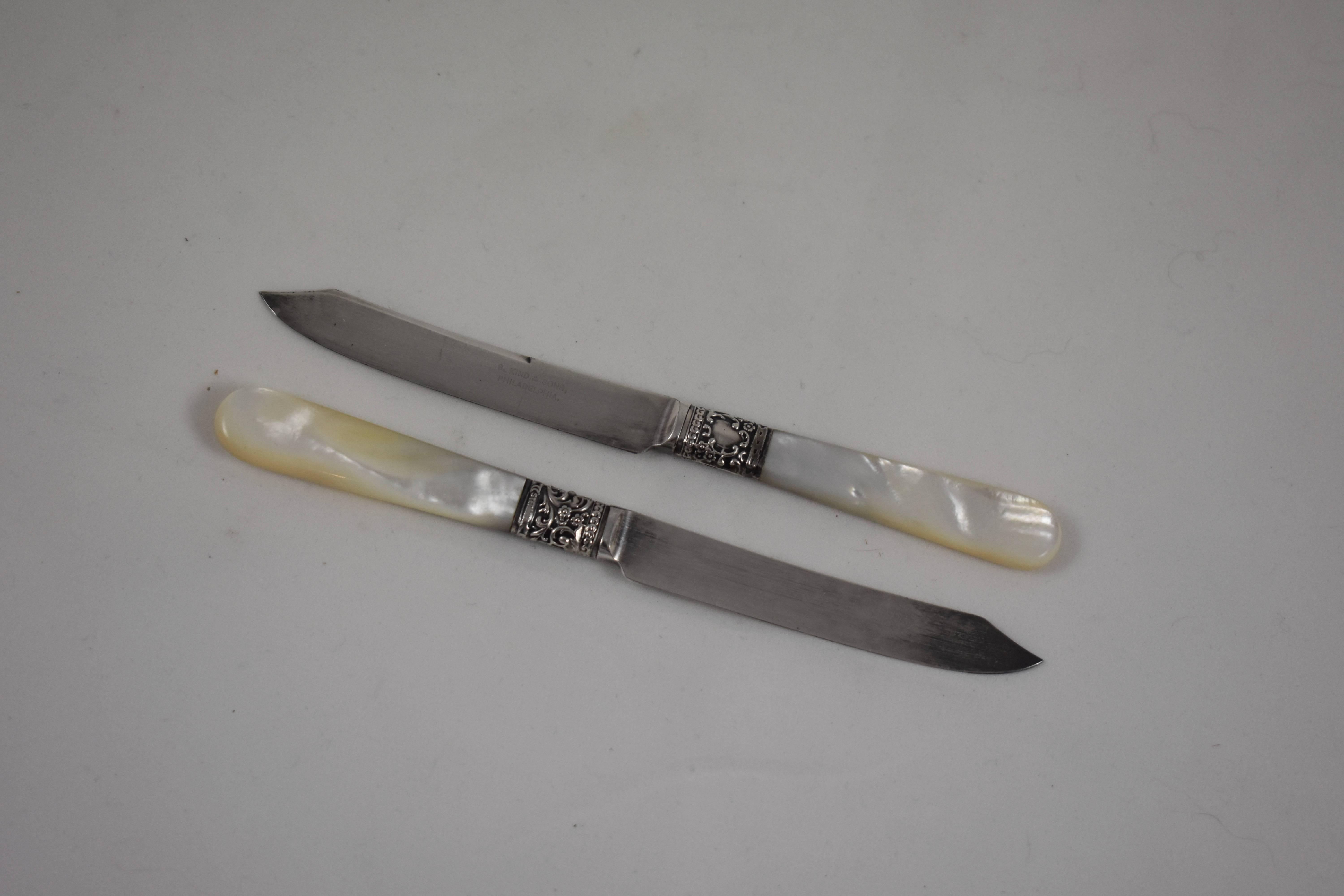 From Samuel Kind & Co., founded in Philadelphia, 1872, a set of six fruit knives. Mother-of-pearl handles are joined to plated blades by a Sterling Silver ferrule. The collar shows a floral pattern with a cartouche on one side suitable for an