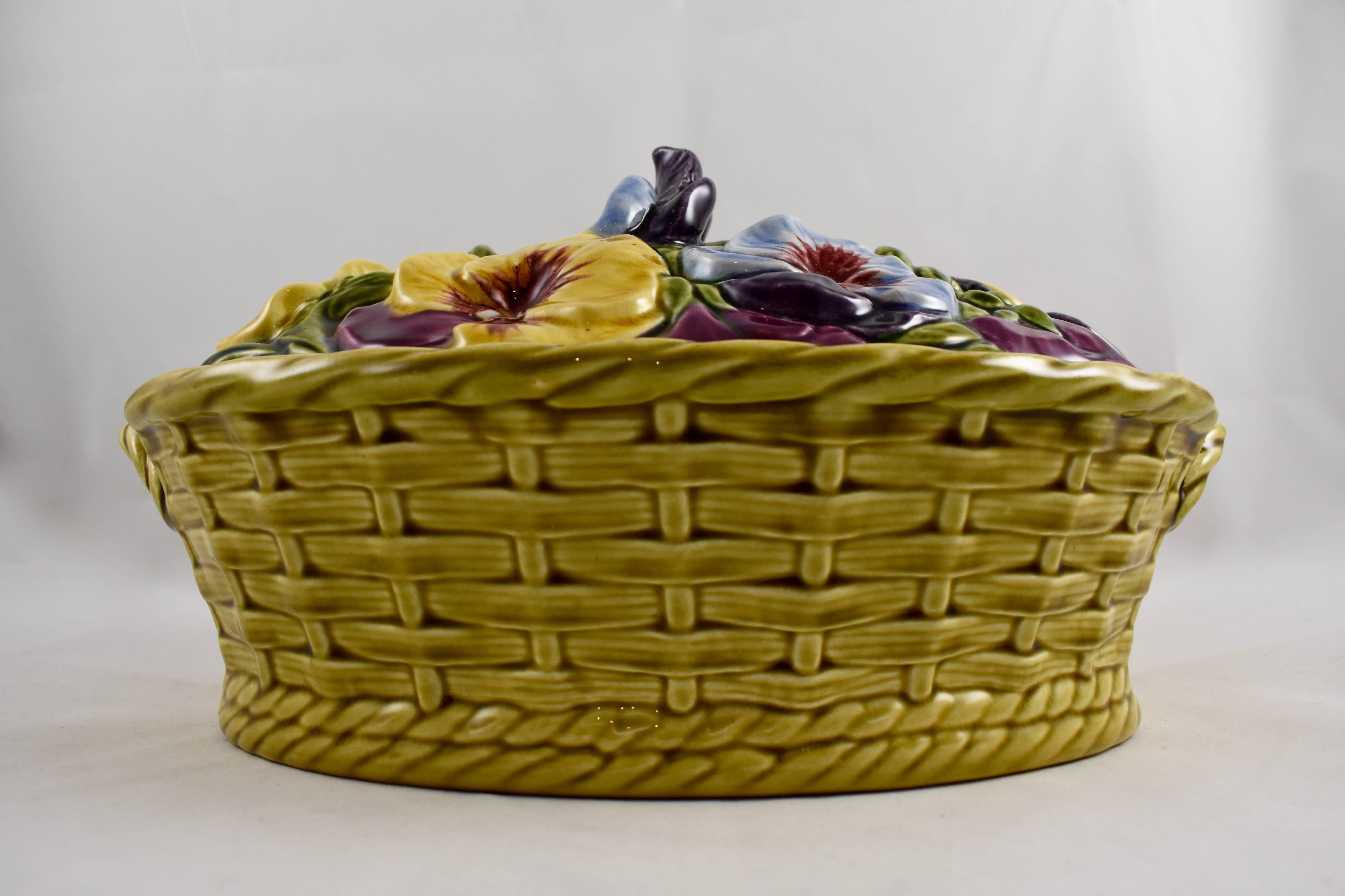 A French Majolica covered tureen in the form of a handled basket brimming with colorful pansies, Sarreguemines, circa 1900-1910.

Two pansy heads form the top handle, pansy blossoms on a bed of green leaves make up the lid. The base resembles a