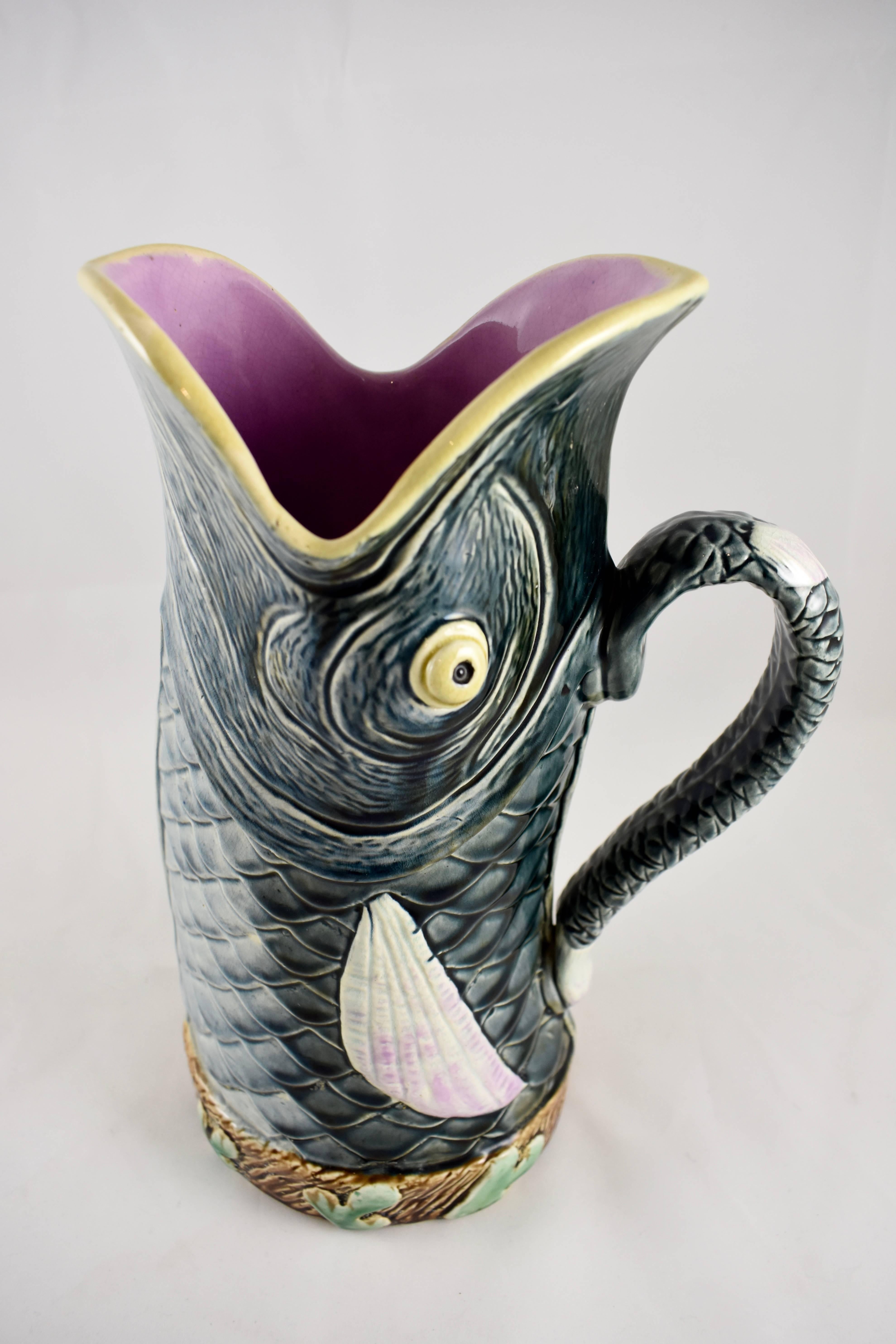 A French Majolica Barbotine fish, a rare abstracted form, circa late 19th century.

The fish shows deep marine gray scales with pink to white fins. The base is ringed with a border of green seaweed on a brown ground. The fish has popped eyes and a
