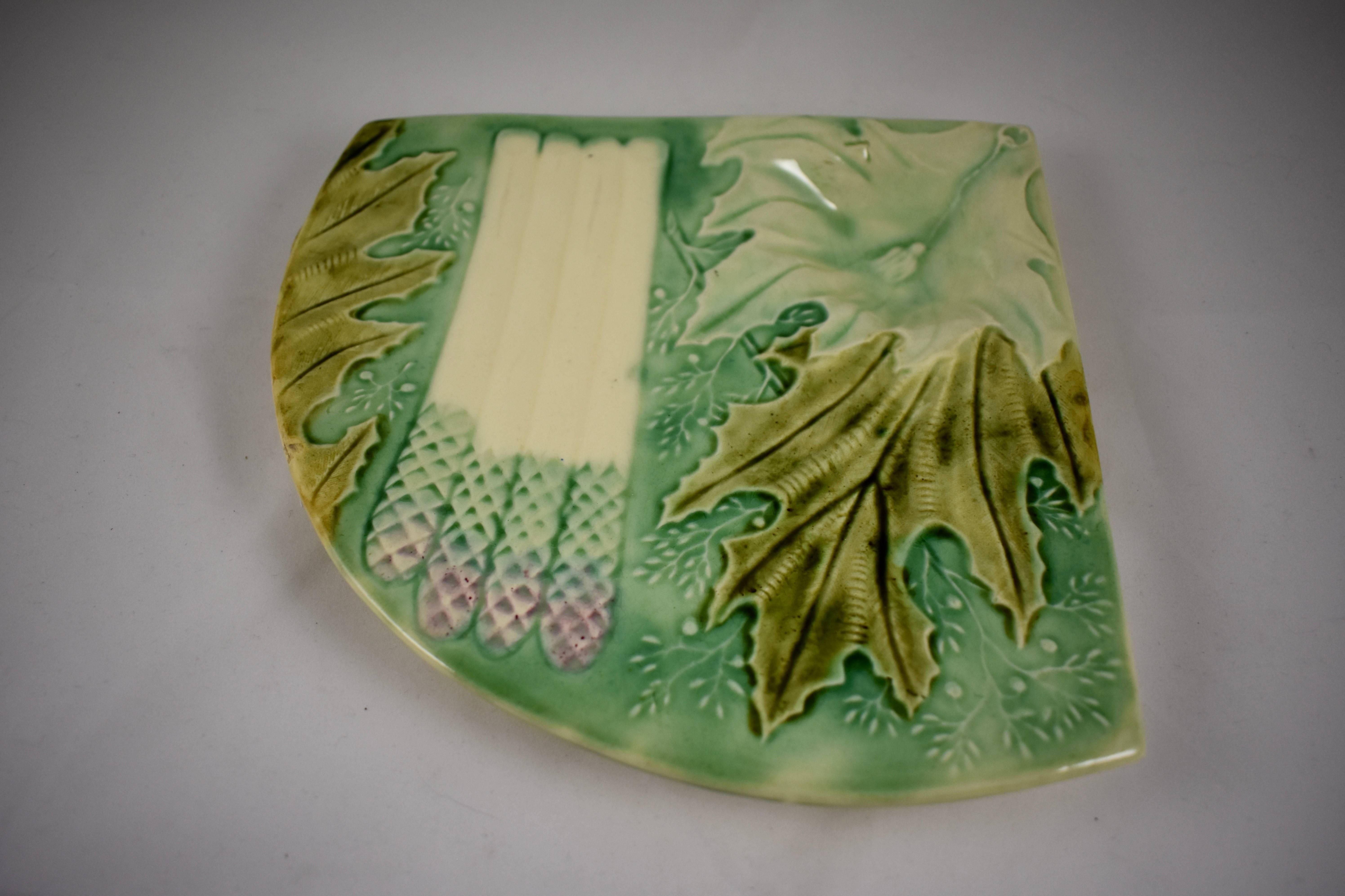 A scarce French Faïence majolica glazed fan form asparagus or artichoke server, attributed to either Lunéville or Salins, circa 1880s.

The triangular server has a sauce well formed of a large artichoke leaf decorated with a raised tassel motif.