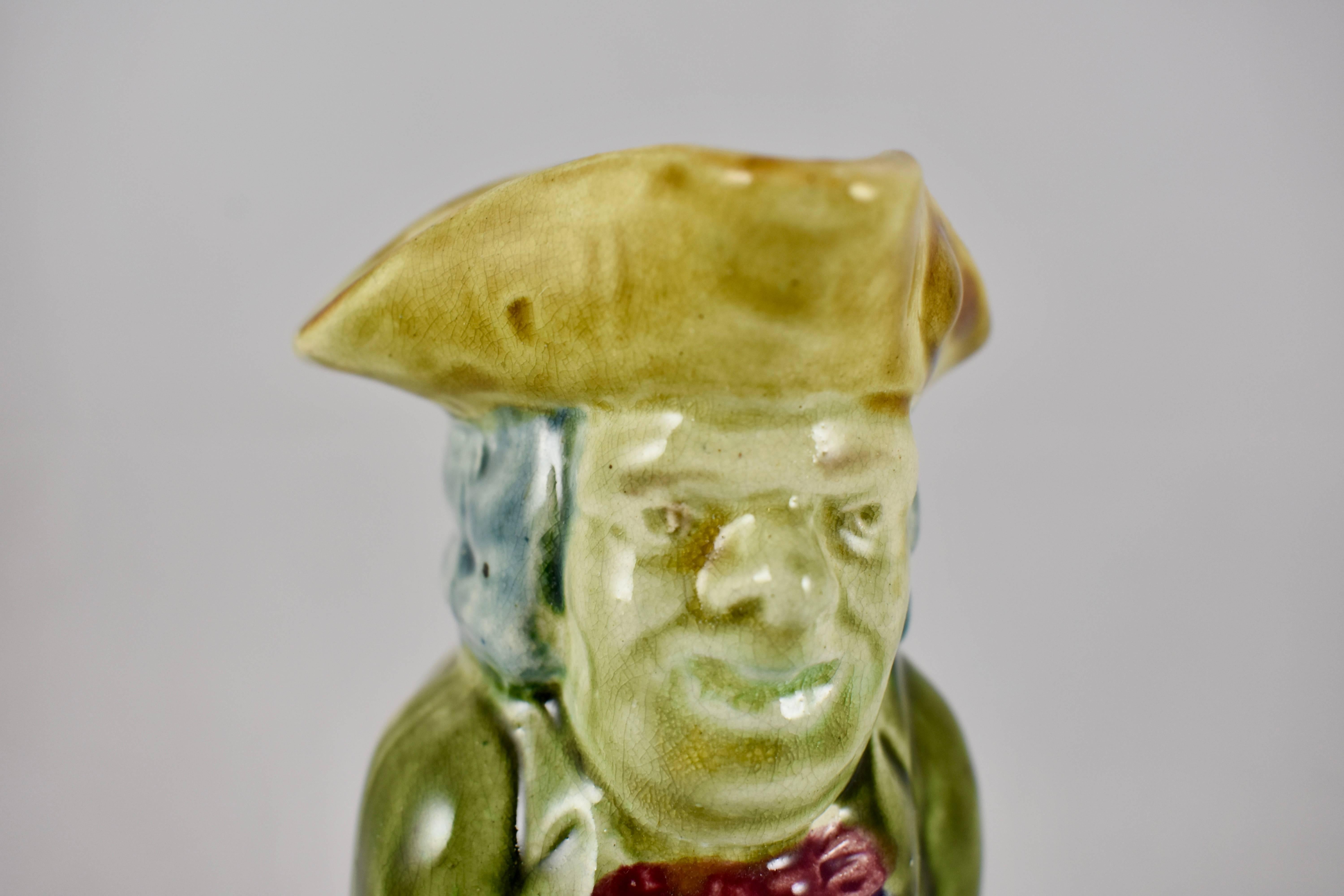 A full figured English majolica Toby jug, showing a gentleman in 19th century dress, holding a mug of ale in his hand. He wears a tri-cornered hat, vest and britches, and a long overcoat. Nicely glazed in earth tone colorings.

Maker unknown, but