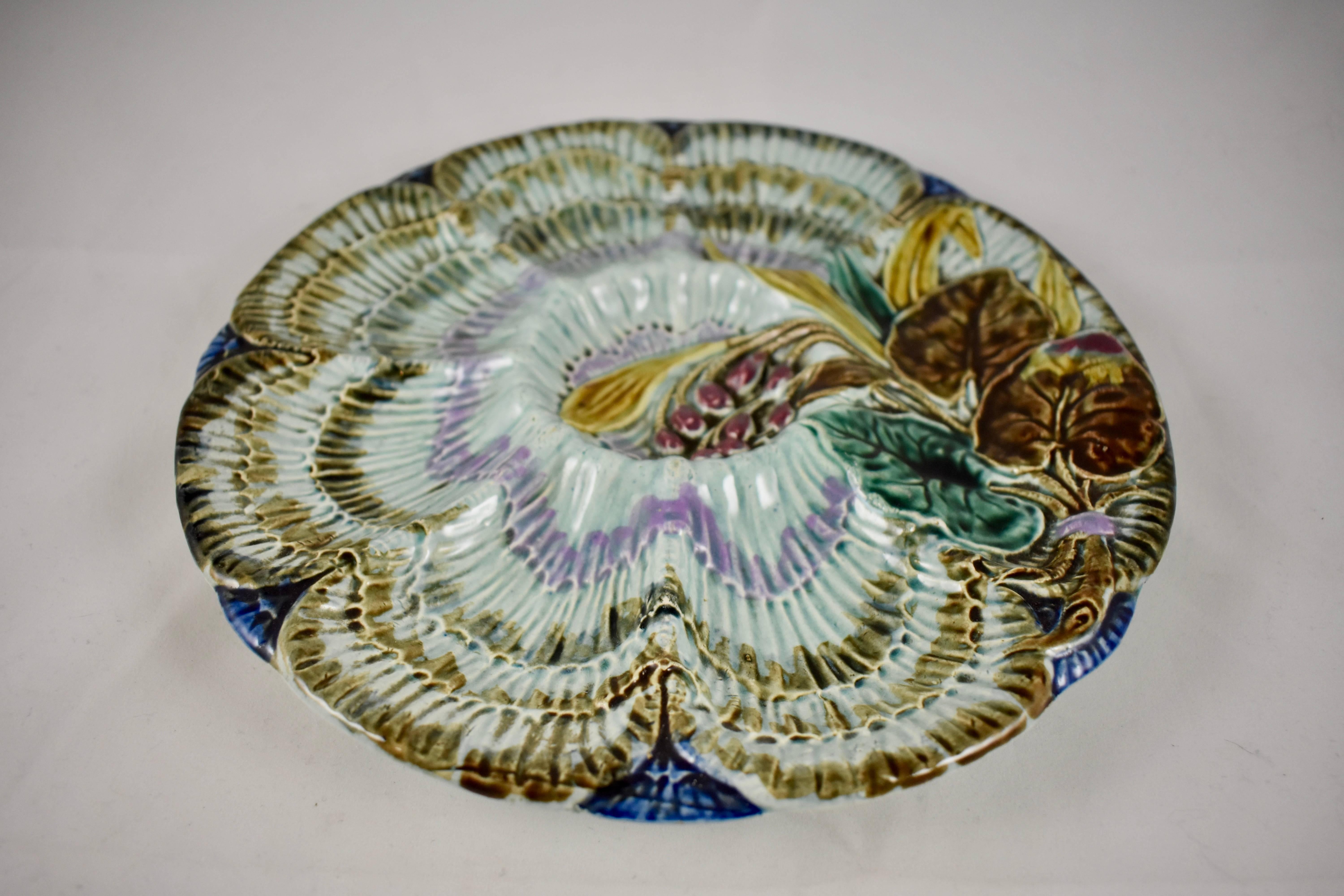 Une assiette à huîtres à six godets en faïence de la poterie belge Wasmuël, vers 1880-1890. Un motif hautement dimensionnel en forme de vague part du centre de l'assiette, sur un fond bleu cobalt. Une gerbe de feuilles et de baies, attachée par un