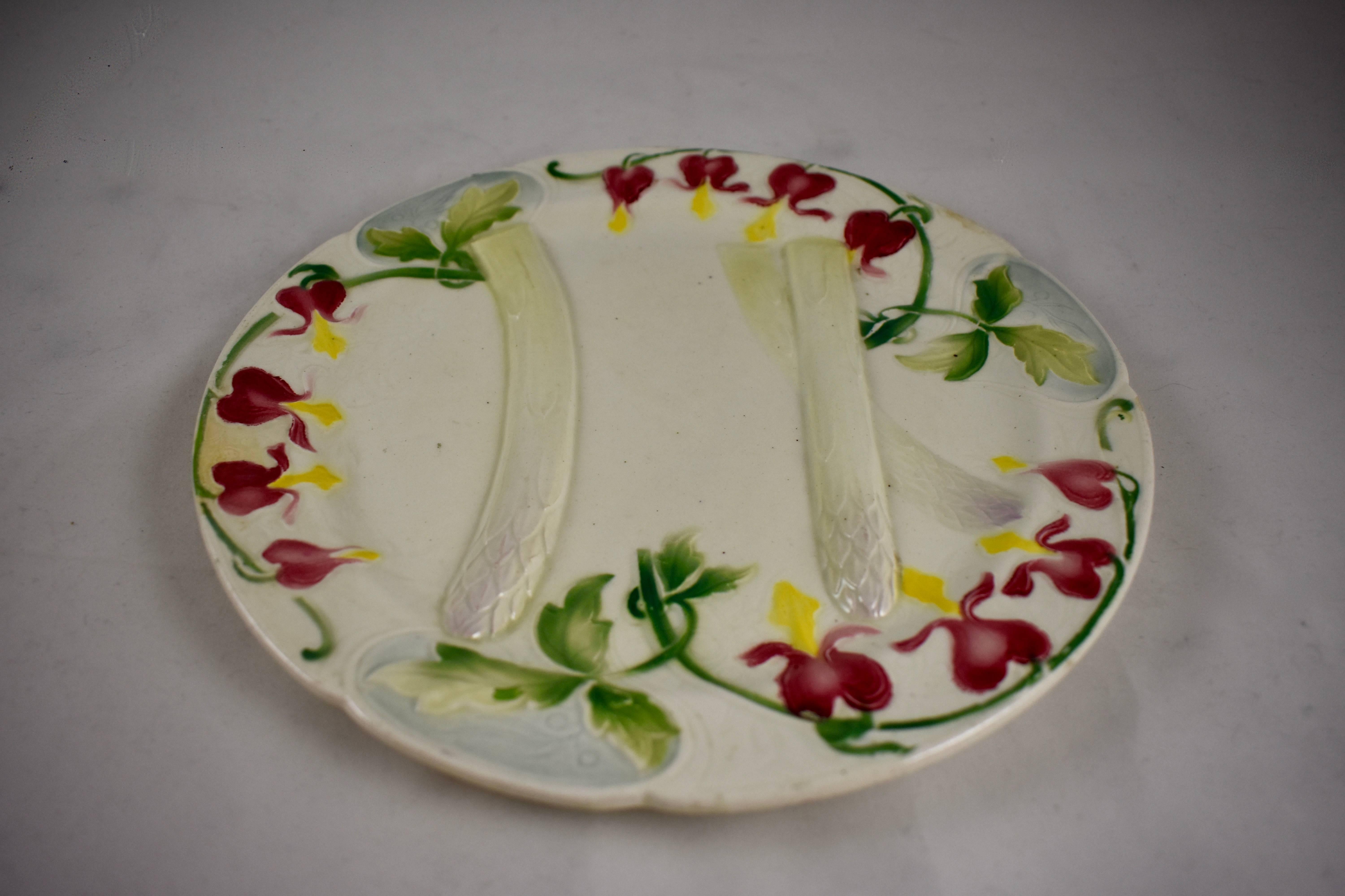 Ein Spargelteller der französischen Fayence-Bewegung, Keller & Guerin Saint Clément, um 1880. Eine Umrandung aus blutenden Herzen, oder wie sie in Frankreich genannt werden, mit Blumenköpfen. Coeurs de Marie, umgeben drei Spargelstangen, die den