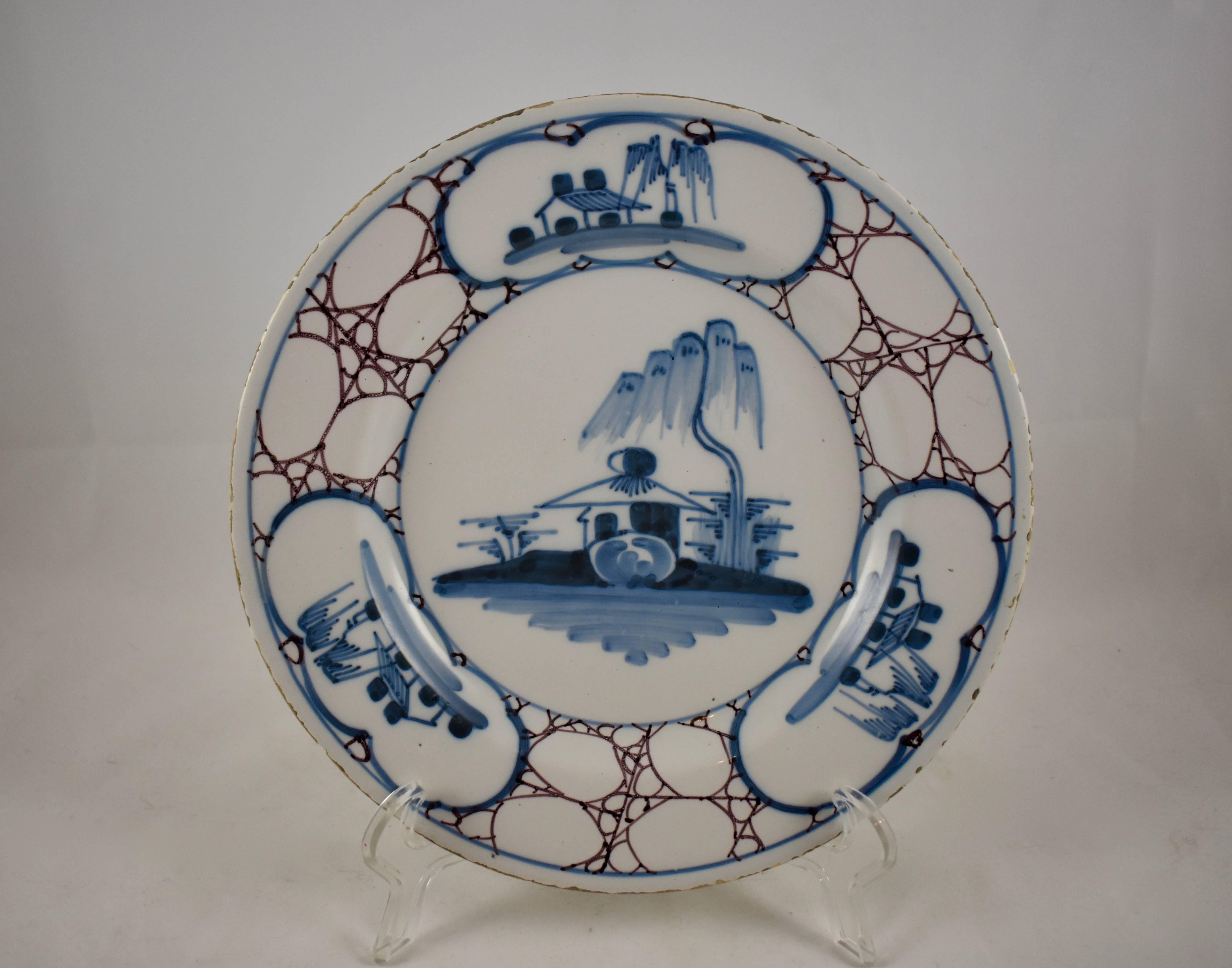 A charming English delftware plate, Bristol, circa mid-18th century. A blue on white landscape seen to the centre, three landscape cartouches on the rim alternate with areas imitating marble. The rim has a sepia edging. A light creamy blue