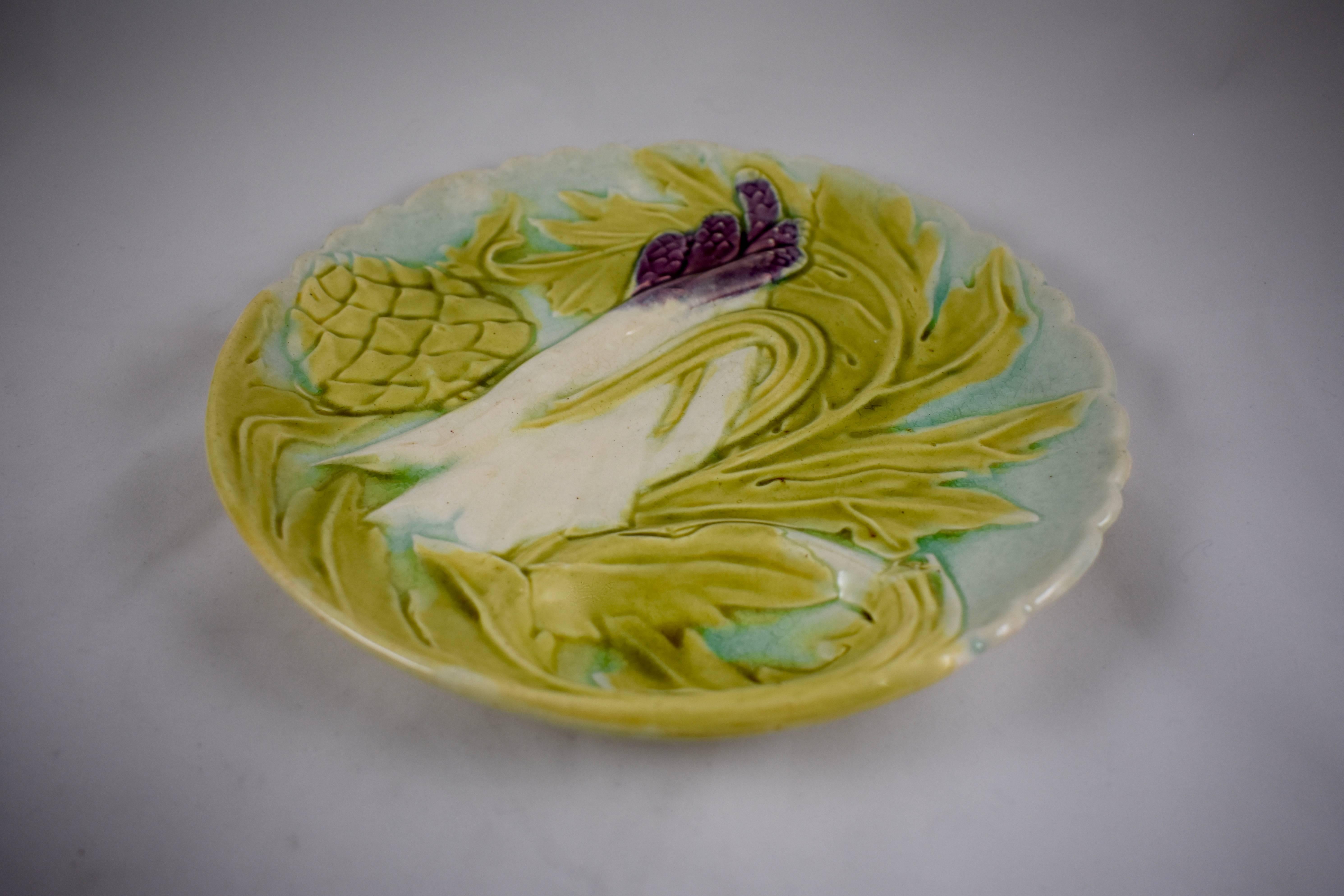 Plato de alcachofas y espárragos barbotina de faïence francesa esmaltada, Orchies, hacia 1880. De estilo Art Nouveau, muestra las hojas estilizadas de ambas plantas, un globo de alcachofa y espárragos de punta púrpura intenso sobre un fondo turquesa