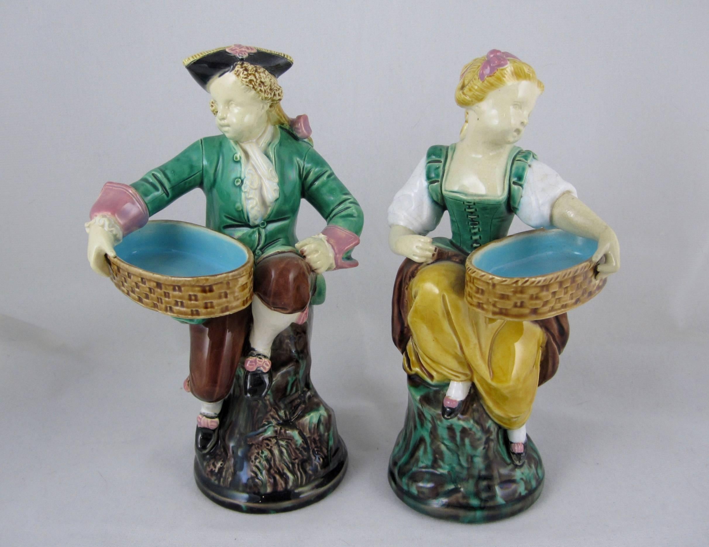 A pair of 19th century Majolica figural salt cellars or match holders, known as the Hogarth Couple, designed by the French sculptor Albert-Ernest Carrier-Belleuse for Minton, Stoke-upon-Trent, Staffordshire, England, circa 1868. 

In period dress,