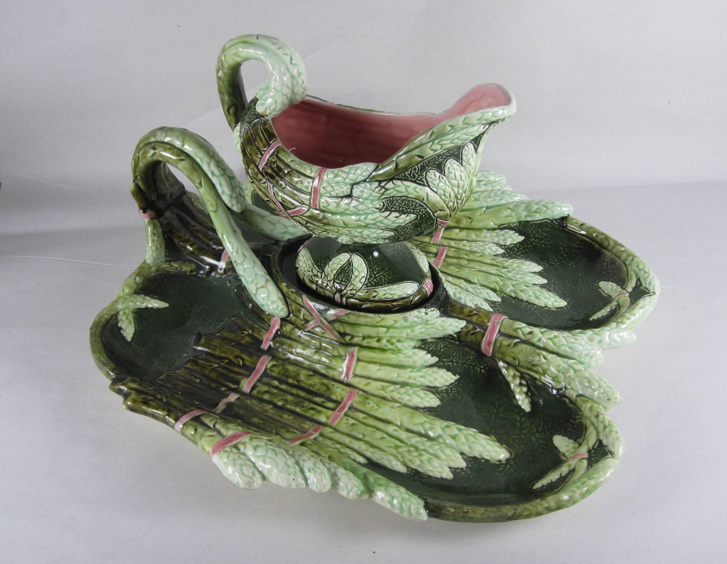 A rare Austrian Art Nouveau-style majolica two piece asparagus serving set, a divided handled platter and a footed sauce boat. Both pieces are molded as ribboned and bent asparagus spears. Marked with the Tower stamp used by Julius Dressler in the