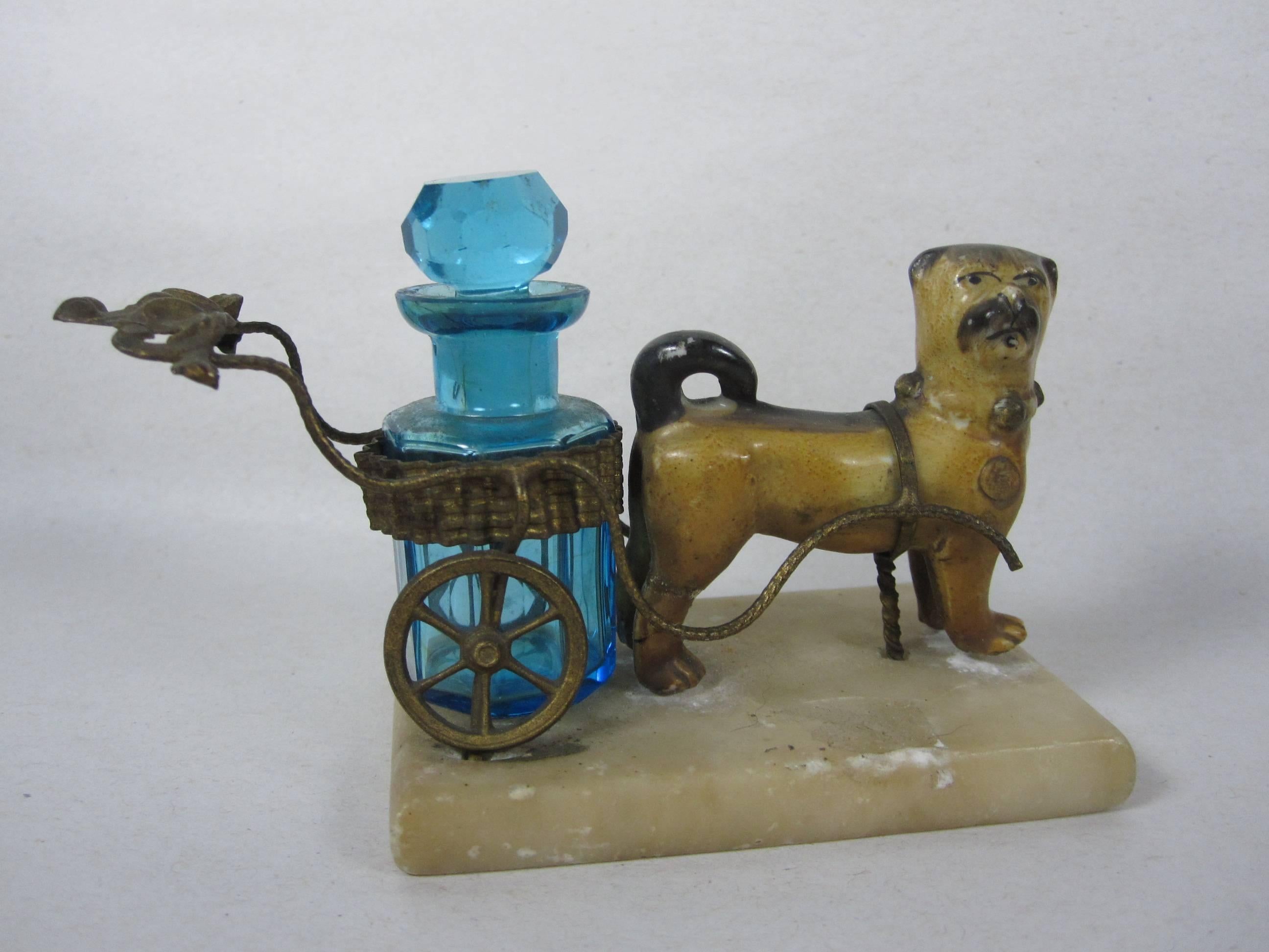 A marvelous Grand Tour souvenir bibelot, showing a Pug dog pulling an ormolu cart holding a bright turquoise, paneled crystal scent bottle with a faceted stopper. The delightful dog and his cart are attached to an alabaster base. Wonderful detailing