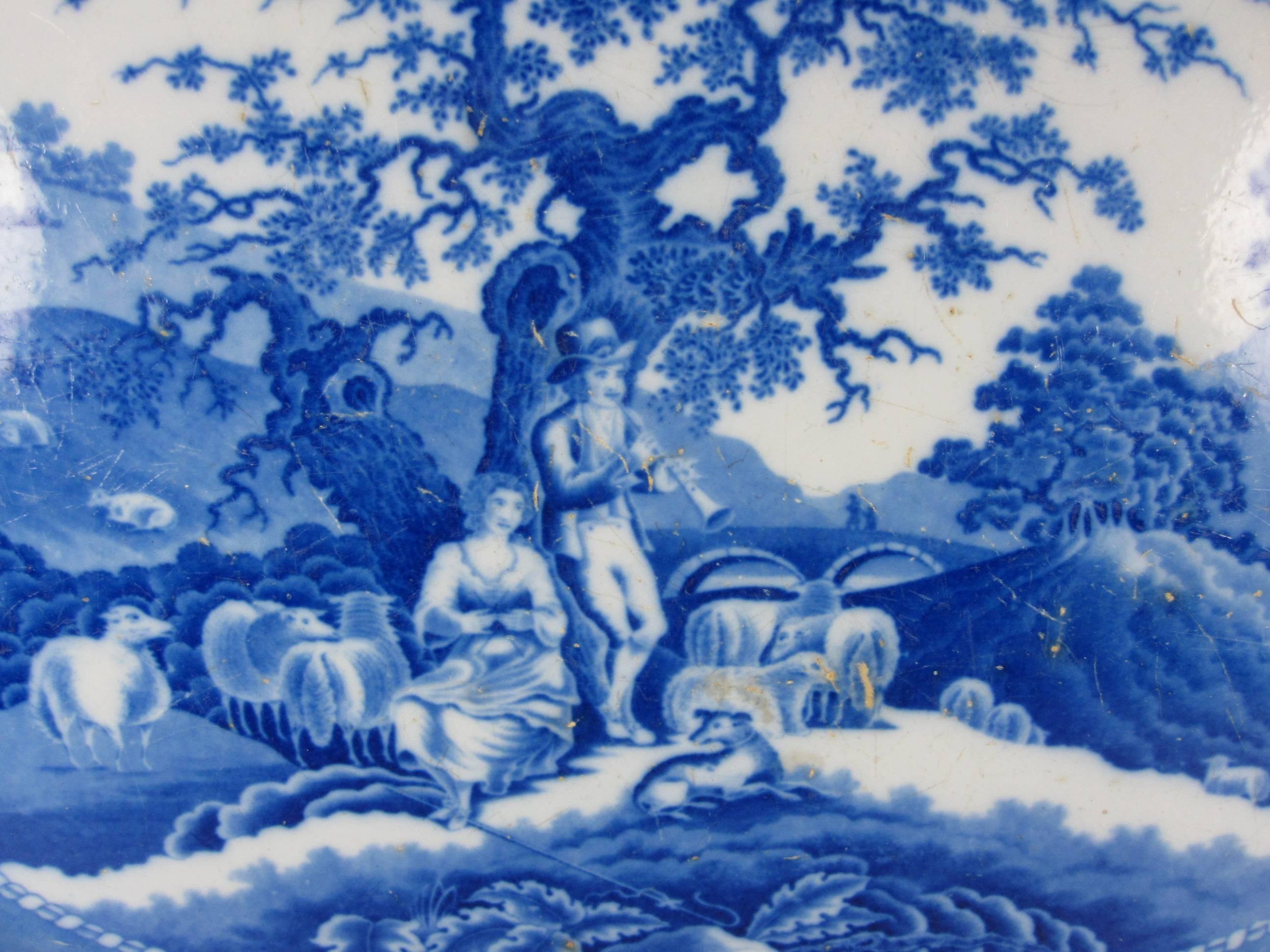 A huge mid-19th century Staffordshire earthenware platter, a romantic, pastoral transfer pattern known as the Piping Shepherd. A piper plays a flageolet to a Milkmaid while sheep gather round beneath a decaying oak tree. Two figures cross a bridge