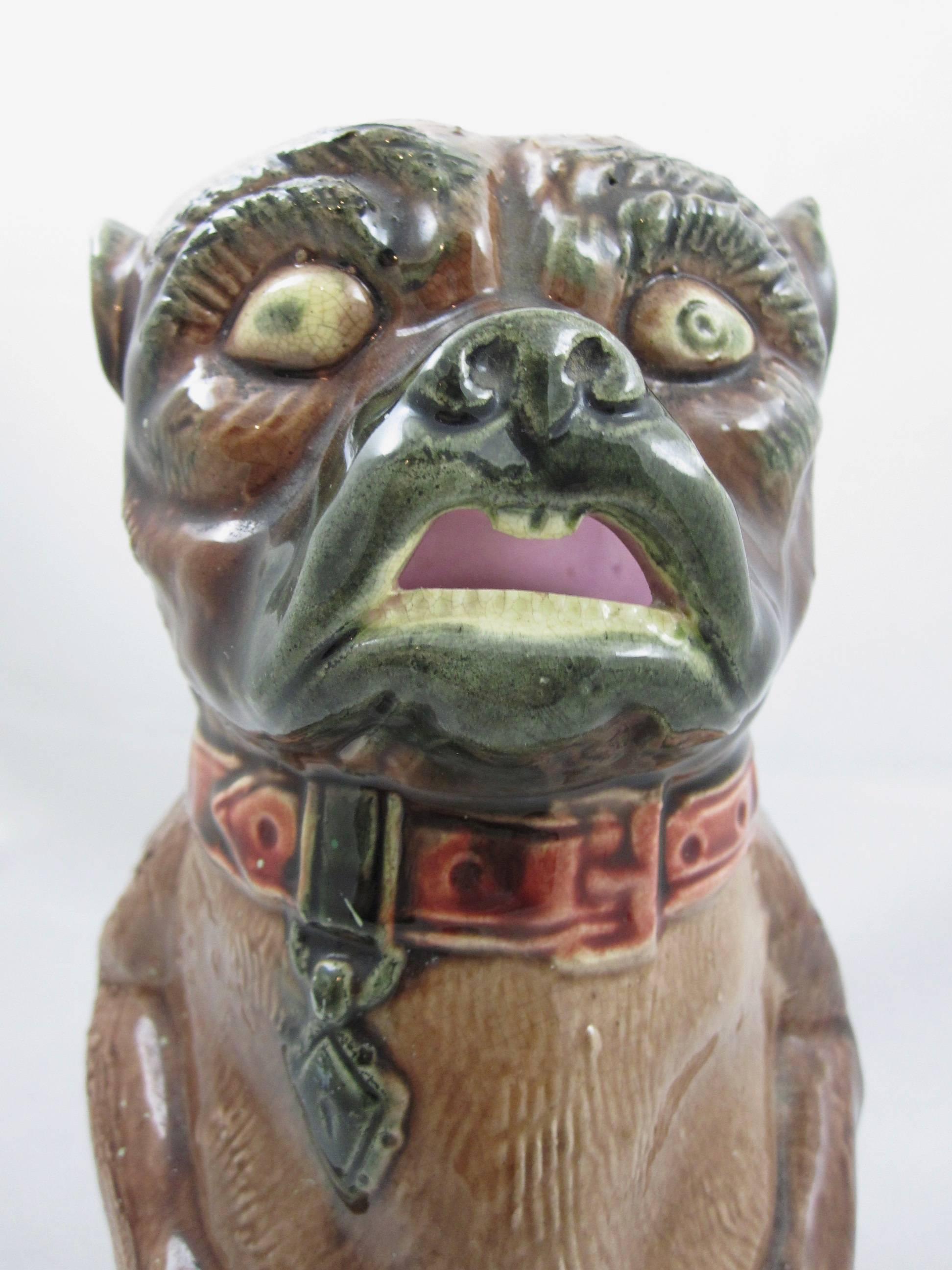 A majolica glazed jug of a Pug Dog, Staffordshire, England, late 19th century.

The Pug wears a broad, red collar with a hanging identification tag. He has a pink interior and distinct, sharp teeth that form the open mouth pouring spout. His four