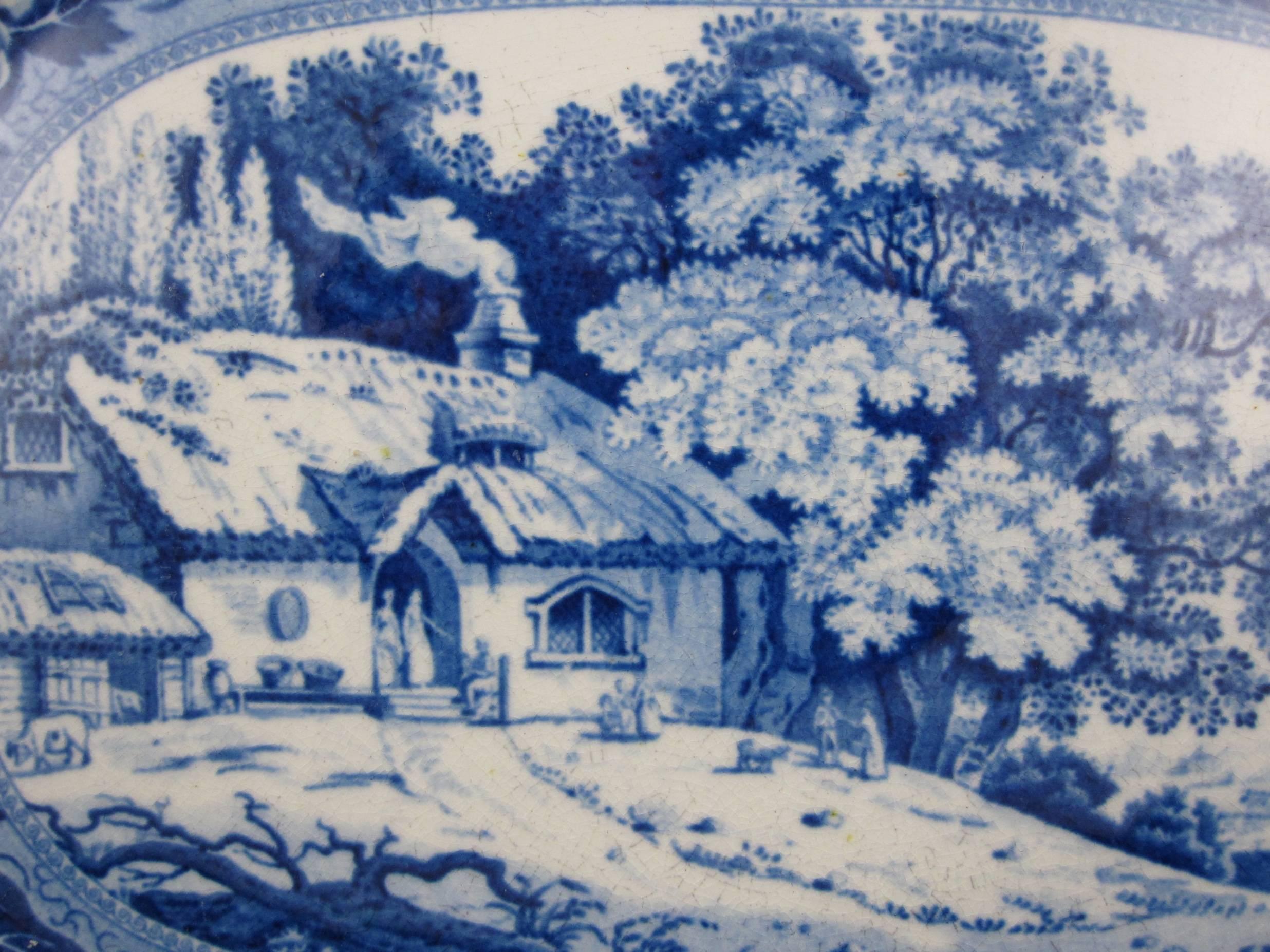 An earthenware, blue and white transfer platter made by Minton, Stoke-on-Trent,
Staffordshire, circa 1820. 

Printed with an image from the “Monk’s Rock” series, this is the family cottage. A thatched cottage with a smoking chimney sits amongst