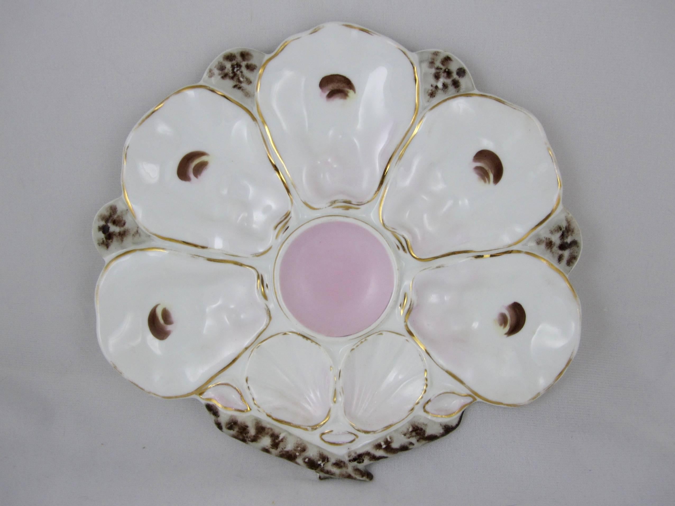 A set of five, shell or fan shaped French porcelain oyster plates, circa 1890-1910.

Five wells with oyster eyes fan out from a center, round condiment well glazed in pink. Two scallop shaped wells sit above a pair of long, mottled and tapered