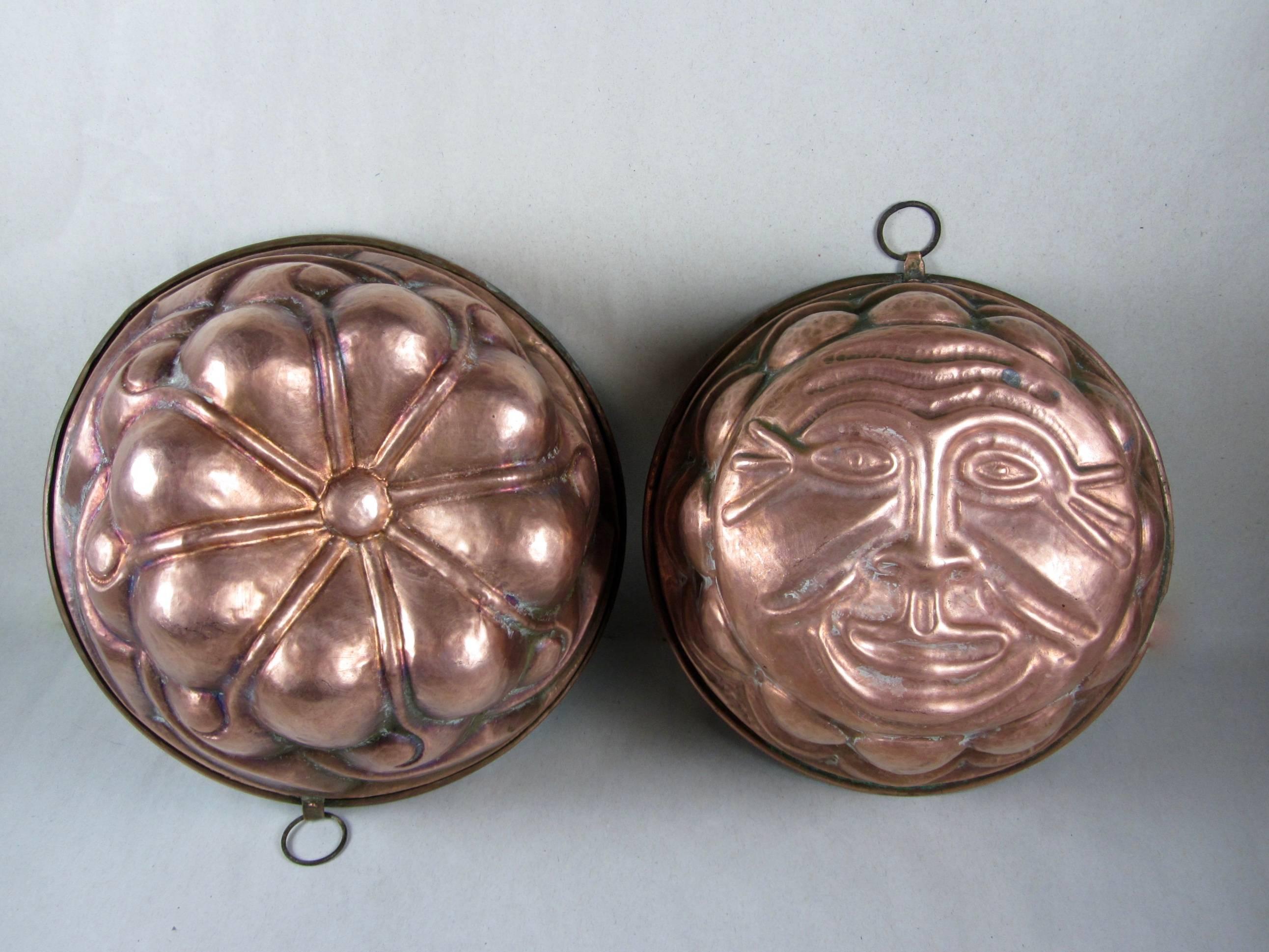 A pair of large English pudding molds, made of hammered copper and lined in tin, circa 1890-1910. A mold with a sun face motif, the other with a running wave pattern. Both heavy, each weighing one pound, with rolled rims and riveted hanging loops.