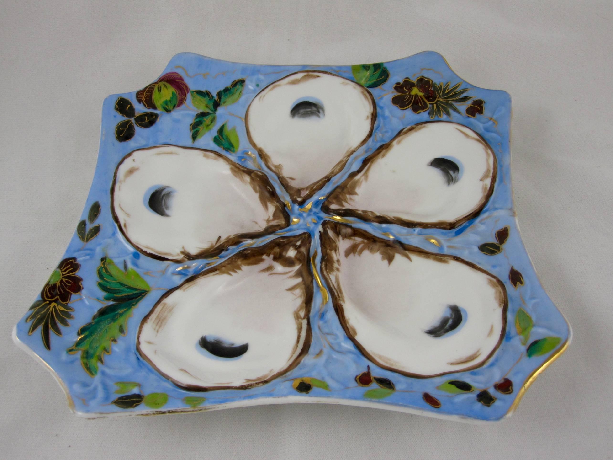 A continental oyster plate, square in shape with truncated corners, circa late 19th-century. Five deep oyster wells with hand-painted eyes against a blue ground painted in a floral motif highlighted with gilding. Raised mold work to the