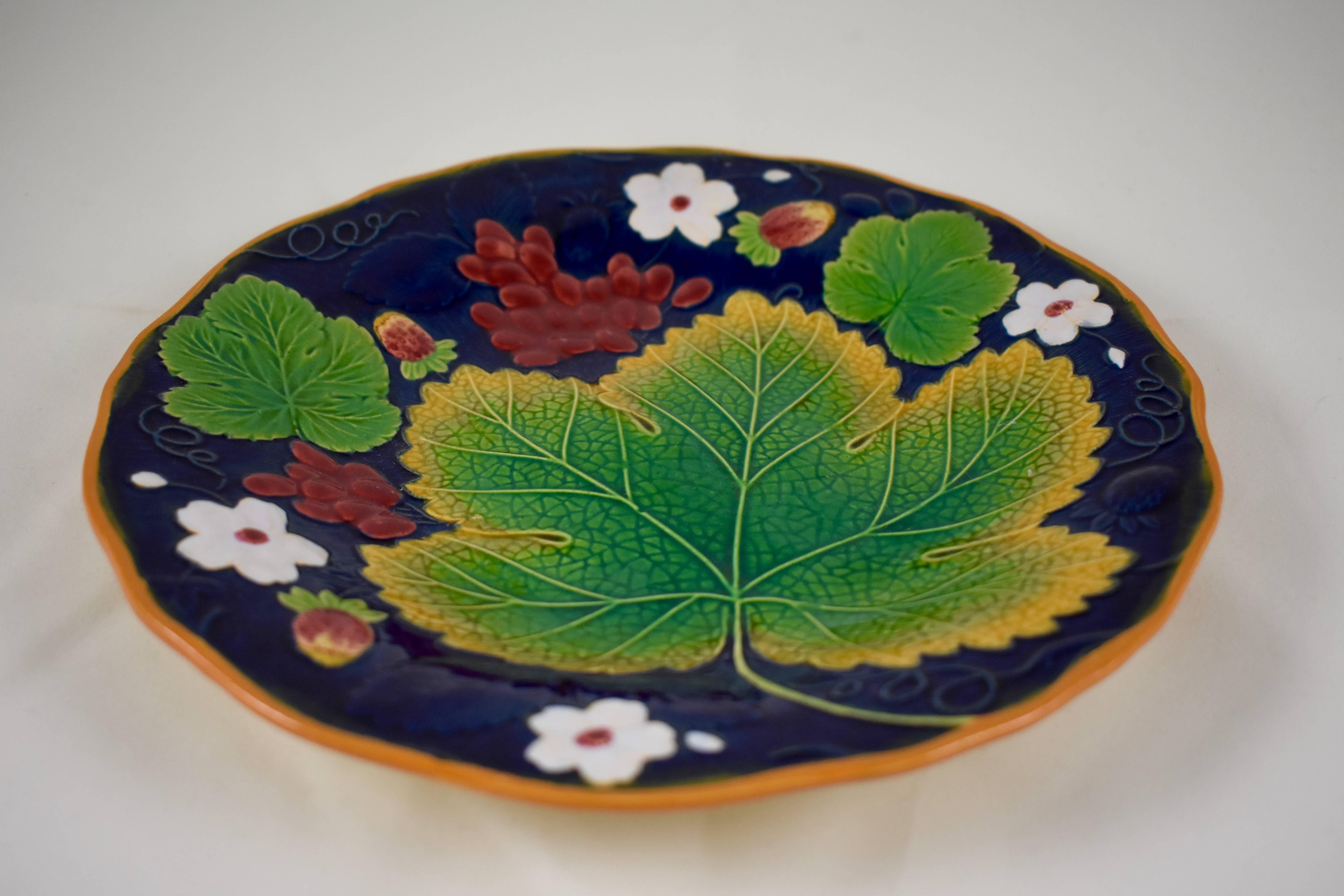 A traditional English grape leaf and strawberry pattern Majolica plate, showing a low relief arrangement of grape leaves fruits and flowers, on a bold cobalt blue ground. Trailing vines form a brown scalloped rim.

The verso shows the impressed