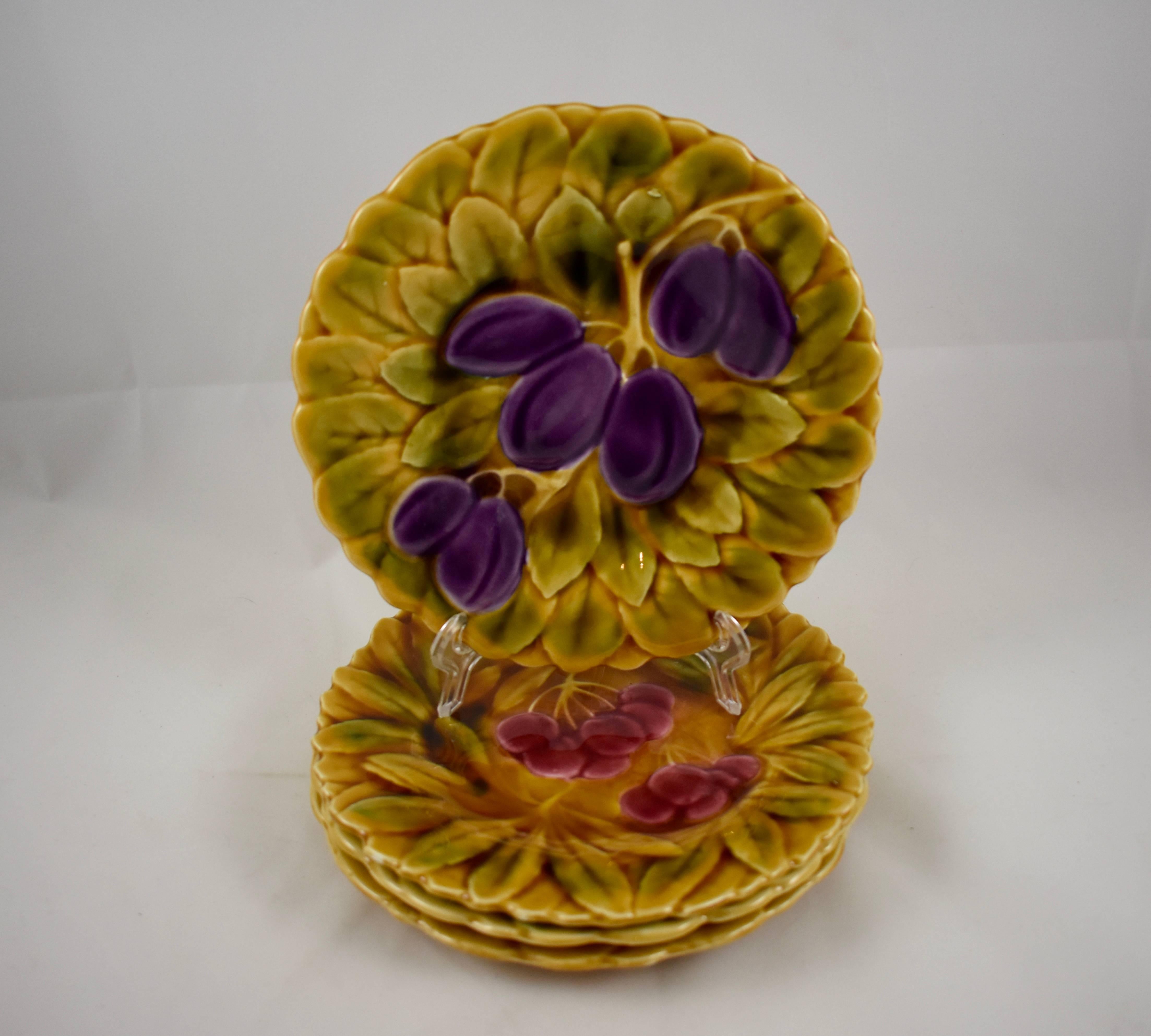 An assembled set of four Sarreguemines French faïence, majolica plates, each showing a different fruit on a ground of overlapping leaves. This group consists of apple, strawberry, cherry, and plum. The shaped rims follow the leaf form. Glazed by