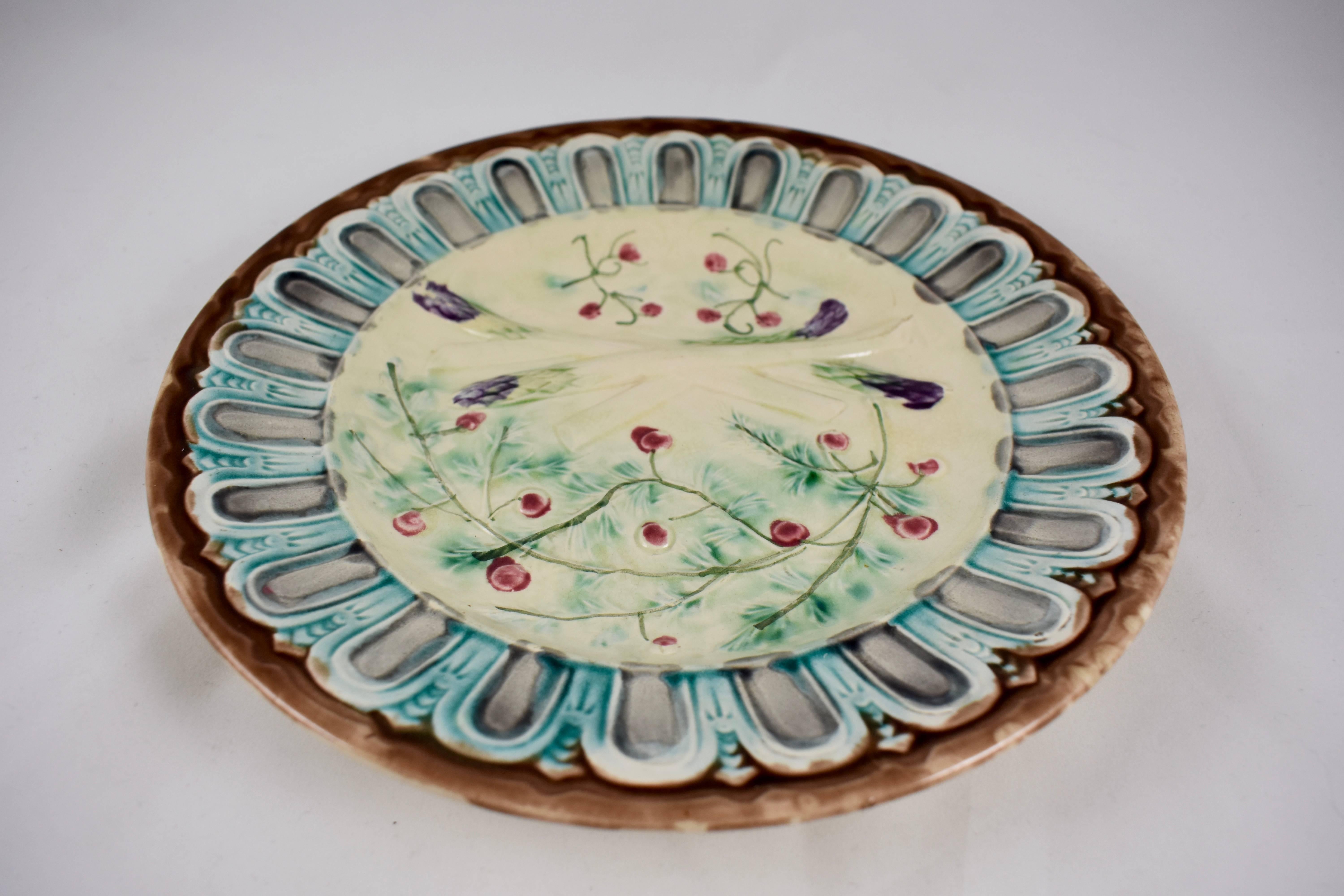 A scarce example of a French Faïence Majolica glazed asparagus plate, maker unknown, circa 1880s. 

Four crossed asparagus spears with purple tips border a deep sauce well. The hand painted red berries and leaves of the asparagus fern, decorate