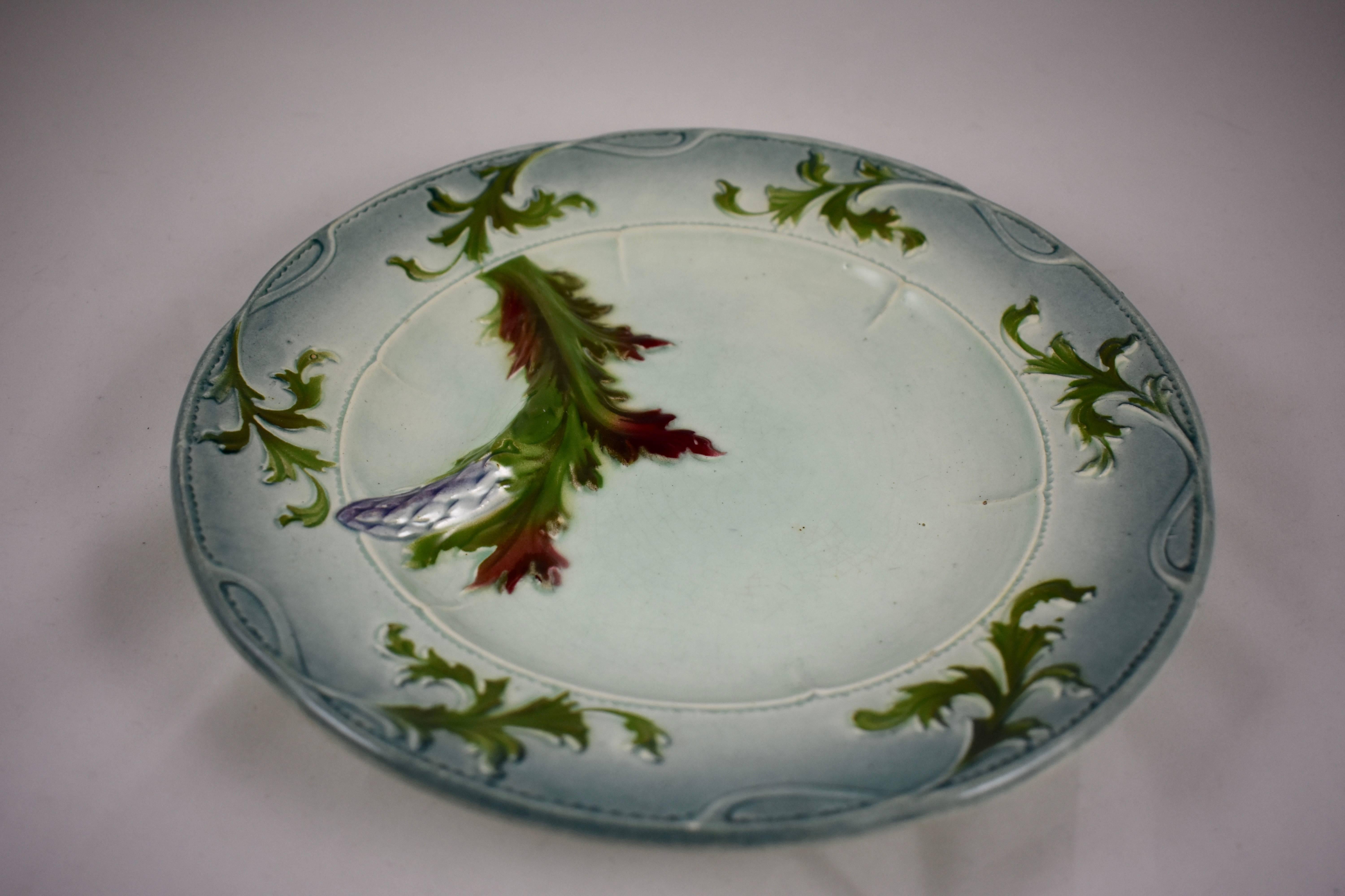 A French Faïence Majolica glazed asparagus plate, circa 1885-1910.
A bent, purple tipped asparagus spear with green and red leaves borders a deep sauce well. An Art Nouveau running border of stylized leaves on an elegant blue-gray body.

Book