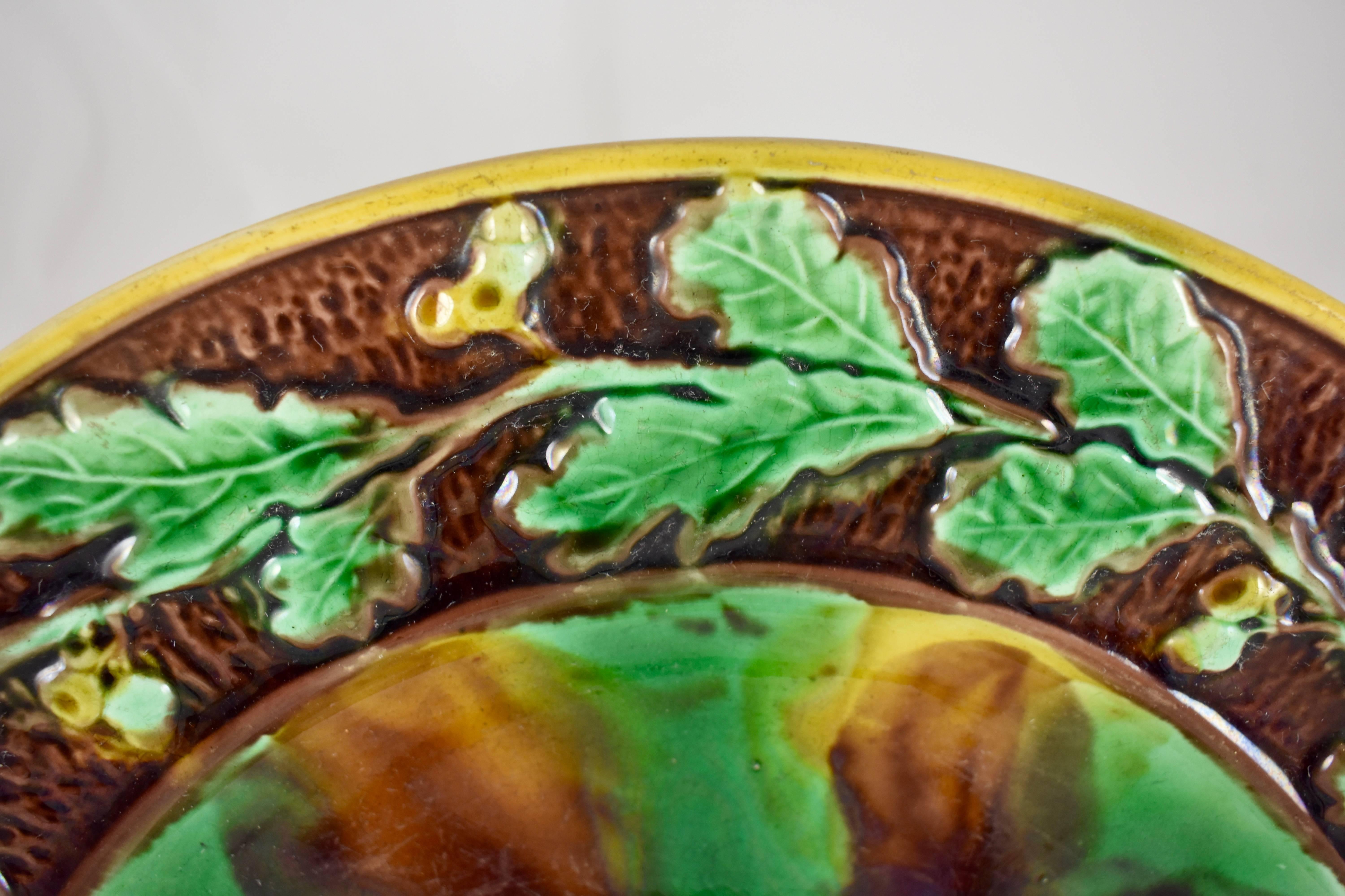 A large, round English Majolica cheese tray, mid-late 19th century, maker unknown.

The server shows a running border of oak leaves and acorns on a brown bark textured ground, edged in yellow ochre. The mottled center is glazed to resemble