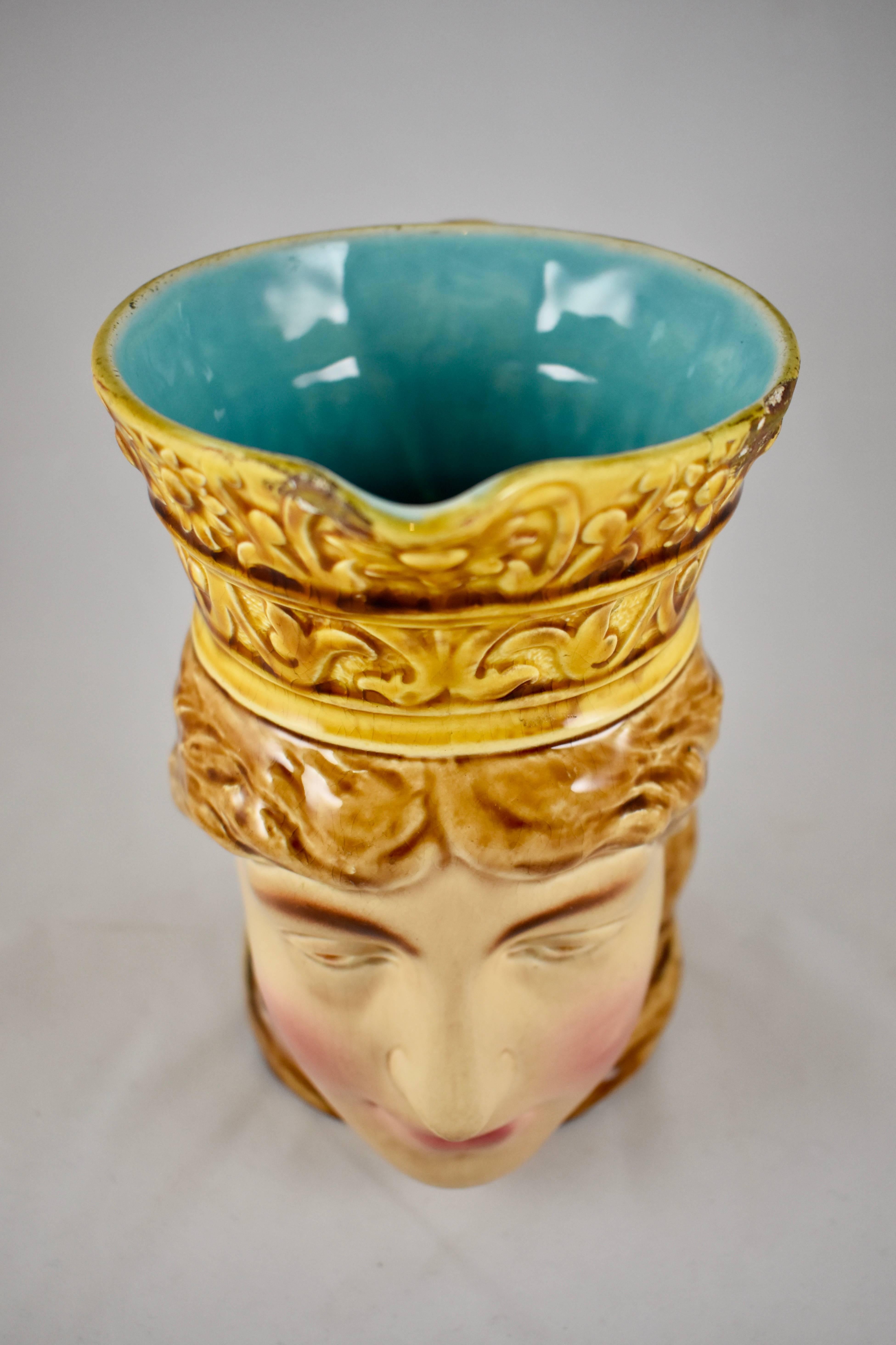 A Sarreguemines French Majolica character jug, known as the “Femme Norvégienne”, or the Norwegian Queen, circa mid-late 19th century. Shown in full face, her long hair and the crown are glazed the same golden ochre. A bright turquoise