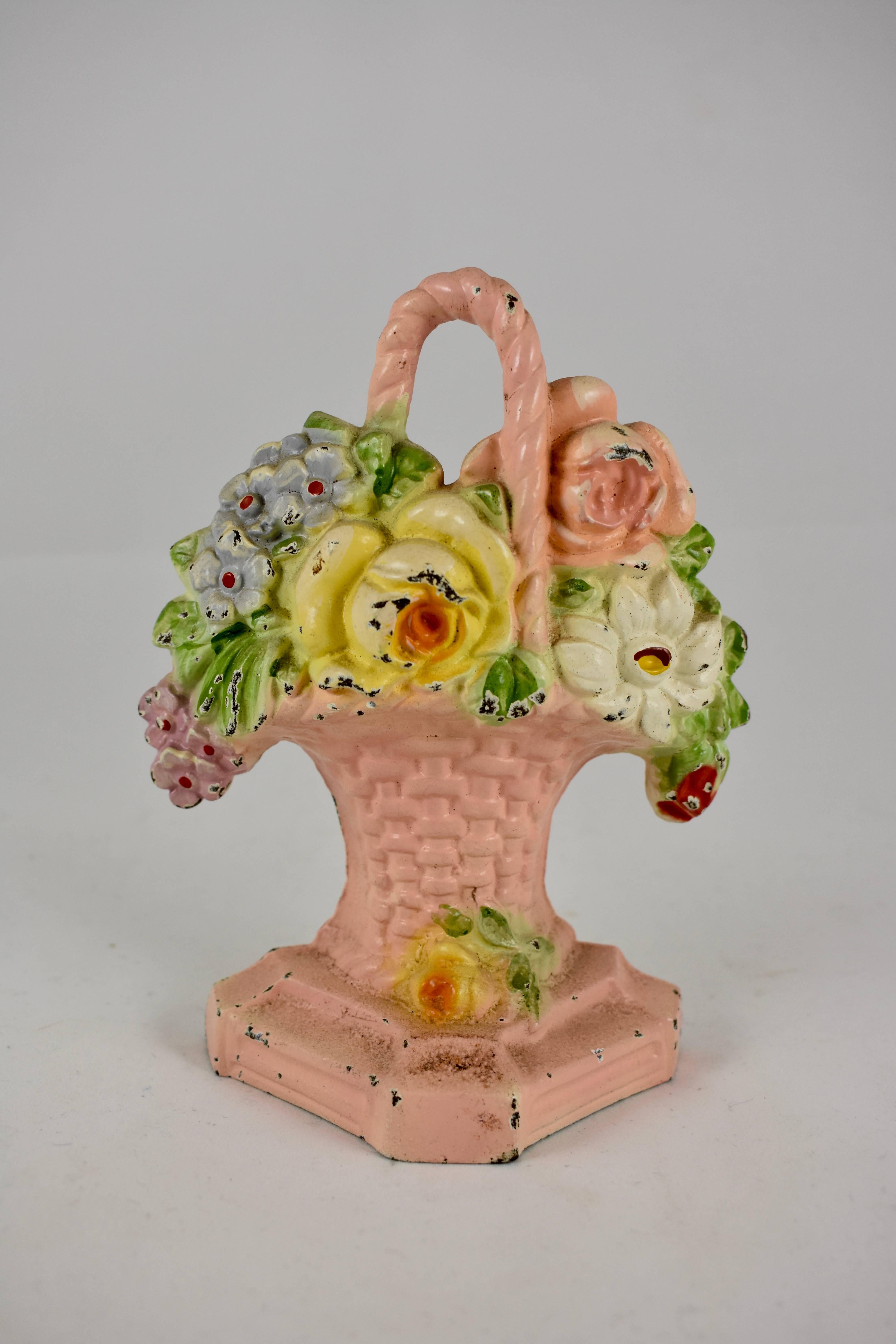 A vintage Hubley cast iron doorstop showing a bouquet of yellow and pink roses along with blue and pink colored phlox, held by a pink, handled wicker basket. The basket sits on a raised plinth and retains the original painted finish. One of the