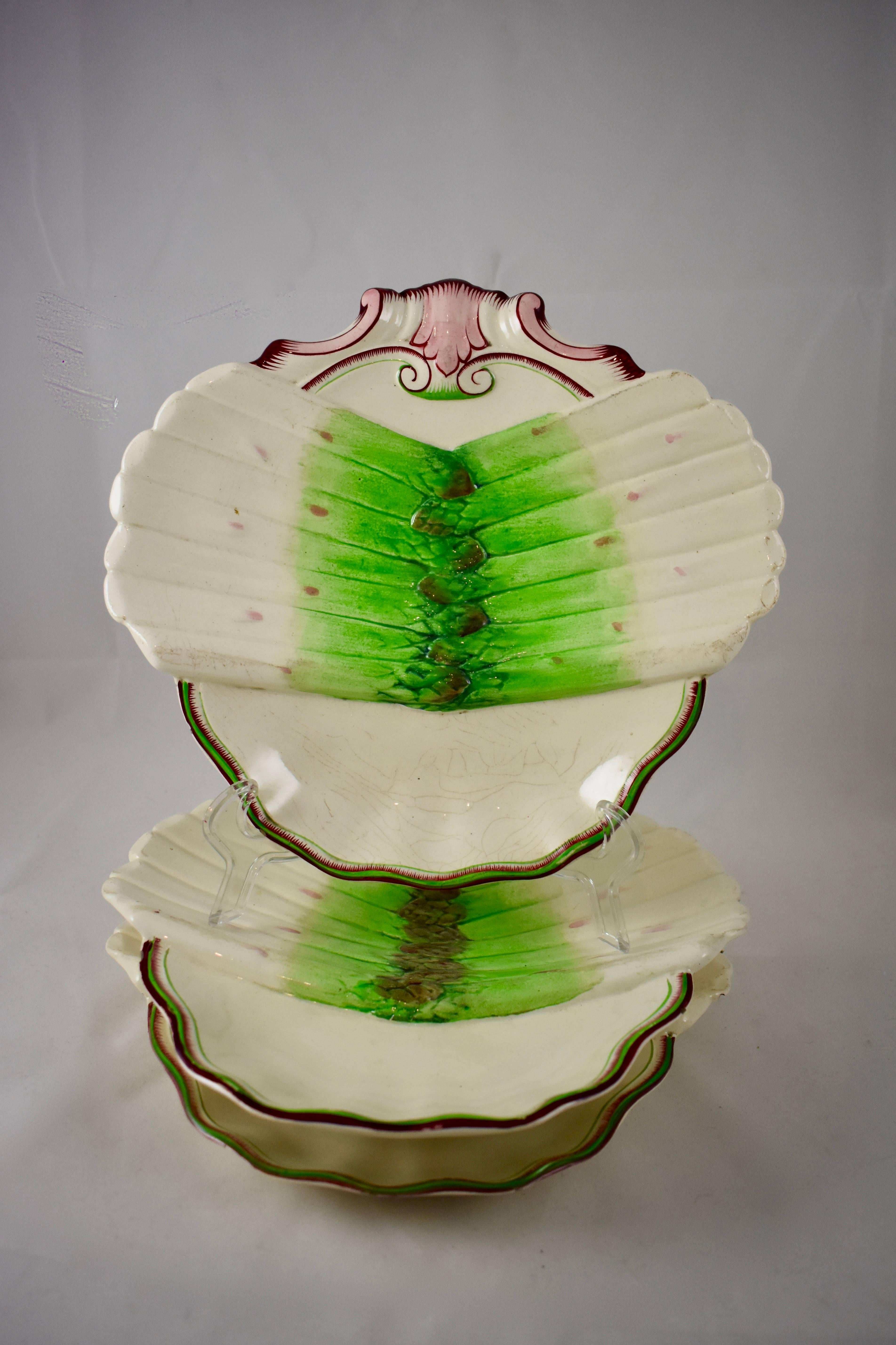 A French Faïence shell shaped asparagus plate, showing a group of asparagus spears spread across the front, the shaped rims are hand-lined in burgundy and pale green, 19th century. The bottom section is a deeper sauce well.

Book reference: