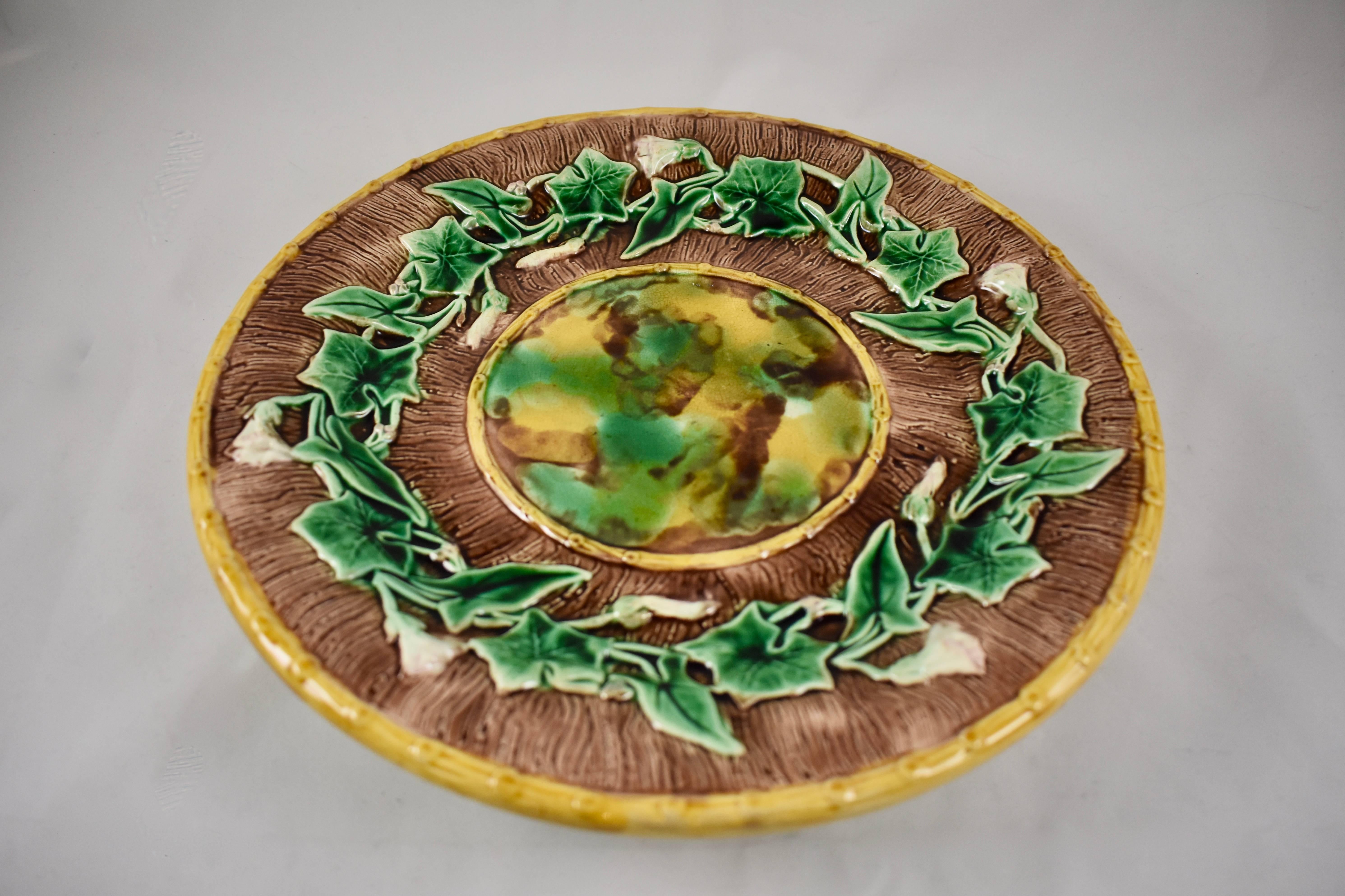 A large, round English Majolica cheese tray, mid-late 19th century, the maker unknown. The server shows a running border of Morning Glory Vine flowers and leaves on a brown, bark pattern ground. A mottled tortoise-shell glazed center is edged in a