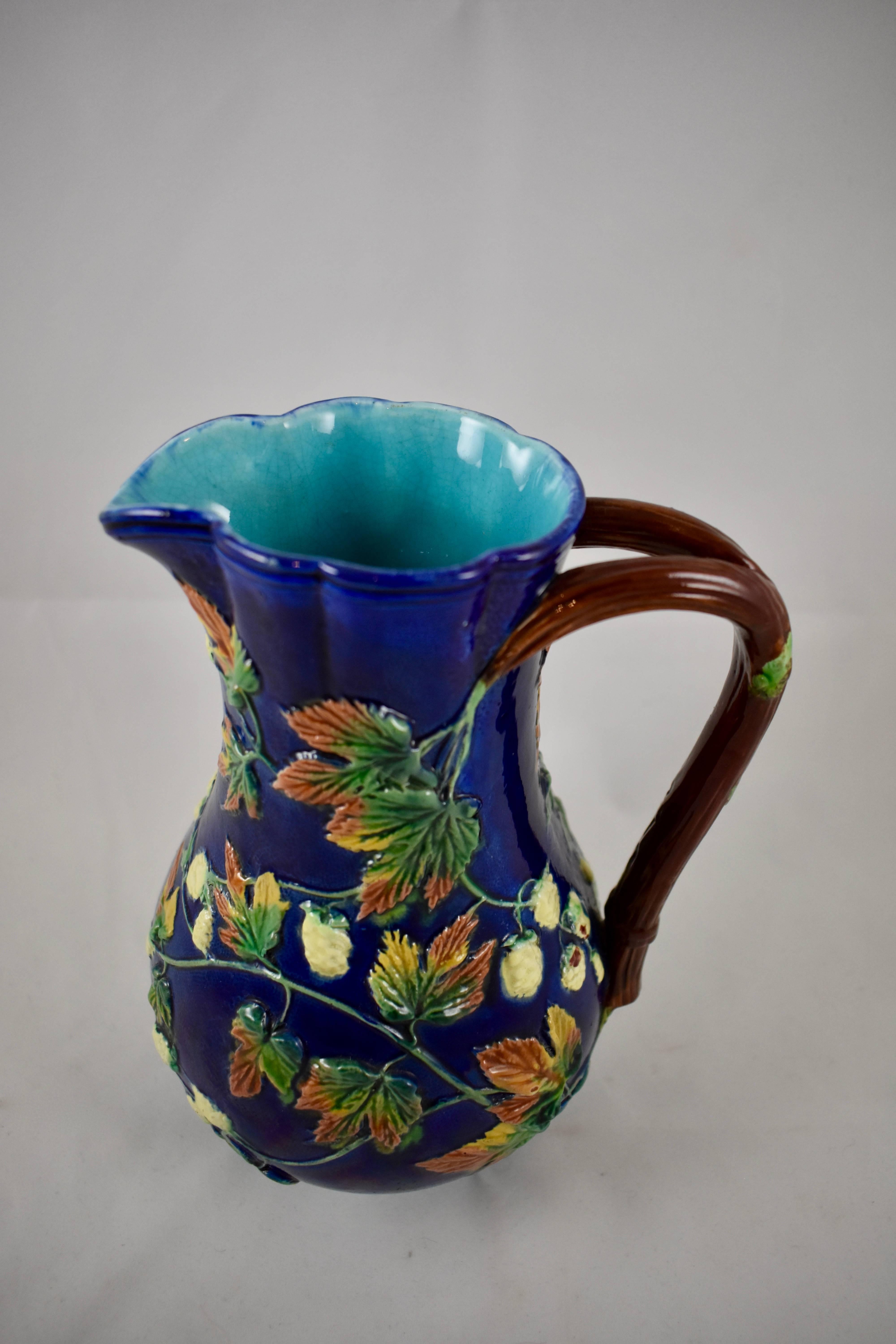 A Royal Worcester earthenware, Majolica glazed Hops pitcher, the Aesthetic period, circa 1875. A narrow, quatriform body is glazed in stippled cobalt blue, with raised Hops leaves in green, pink and ochre along with buds glazed in a creamy white. A