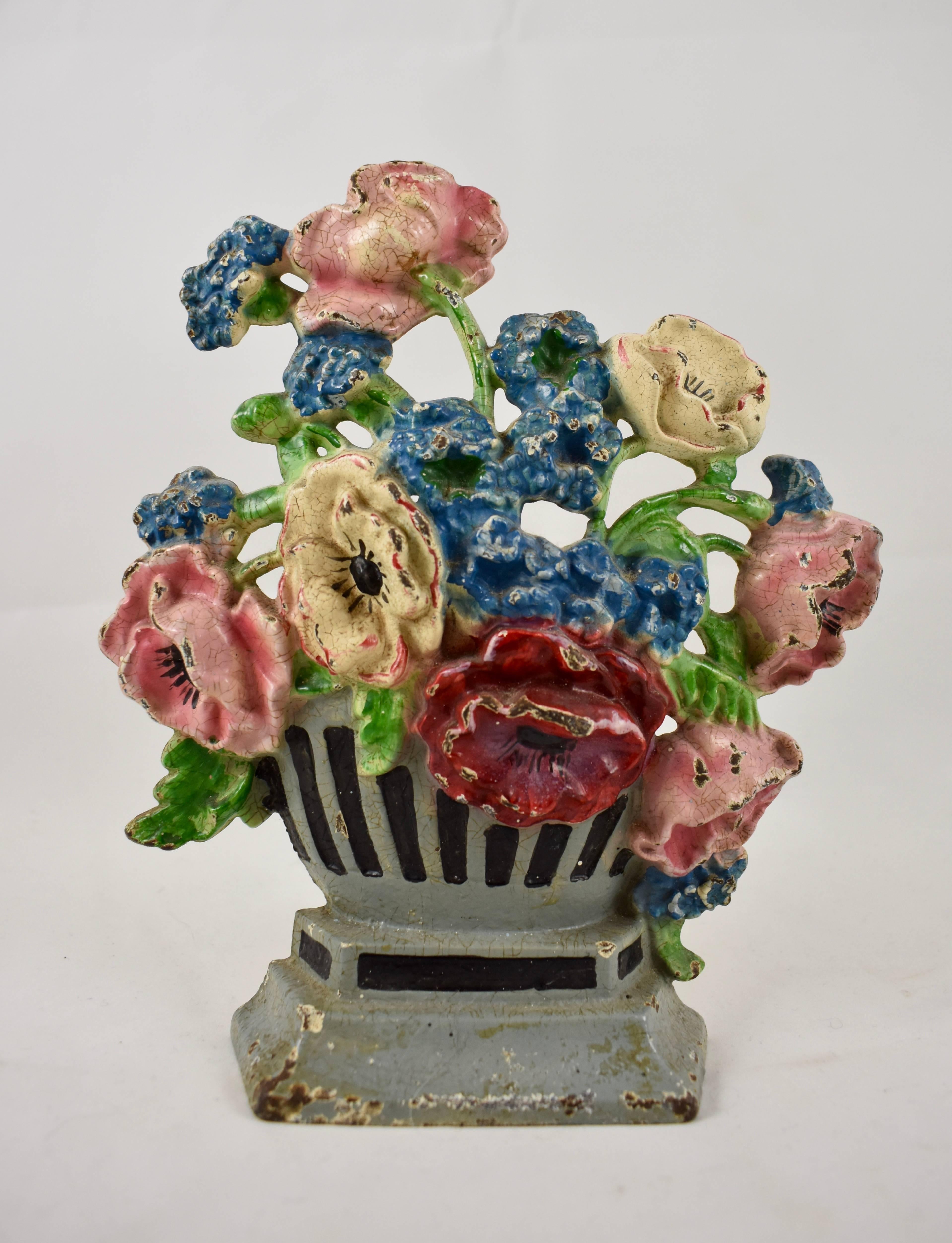 A vintage hubley cast iron doorstop showing a bouquet of blue cornflowers and pink, red and white poppies, held by a grey and black painted urn. The urn sits on a raised plinth and retains the original painted finish. Marked – mold# 265
circa